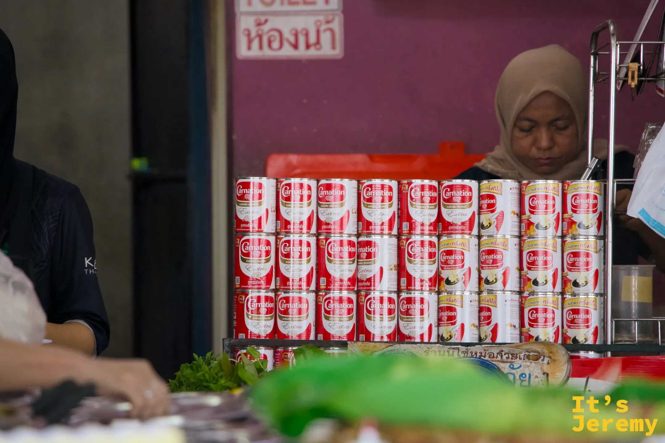 Carnation 煉乳罐整齊堆疊在吧檯旁，是 Teh Tarik 的核心原料