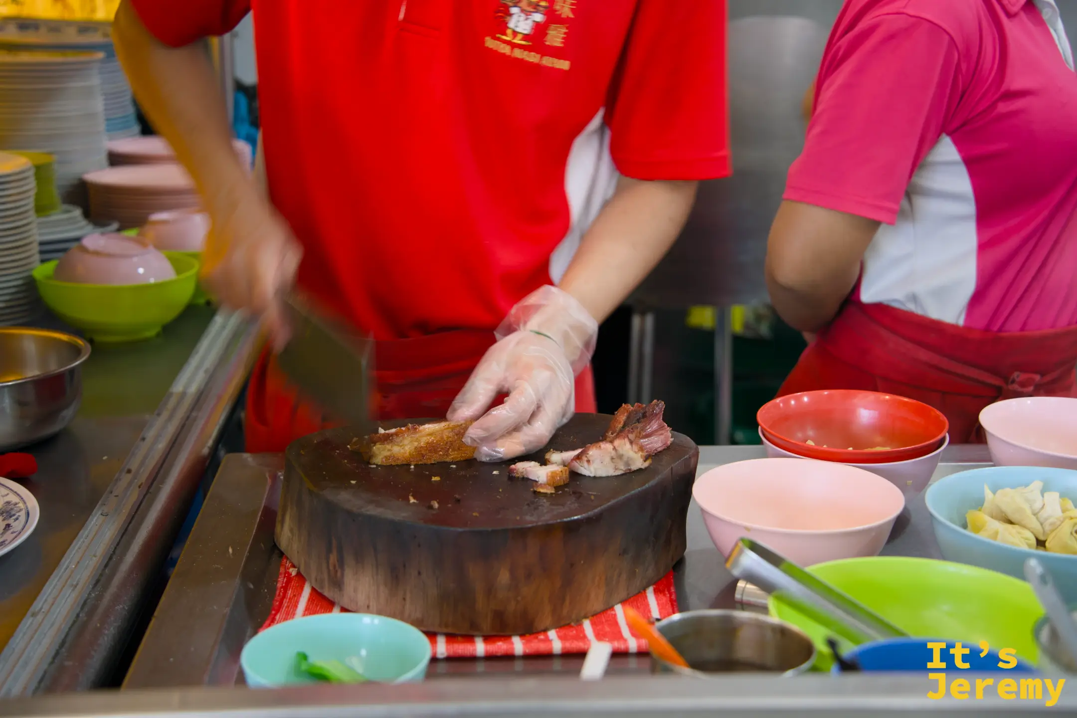 橘色制服員工在大圓木砧板上處理食材，旁邊整排粉紅、珊瑚色與藍色碗盤待命