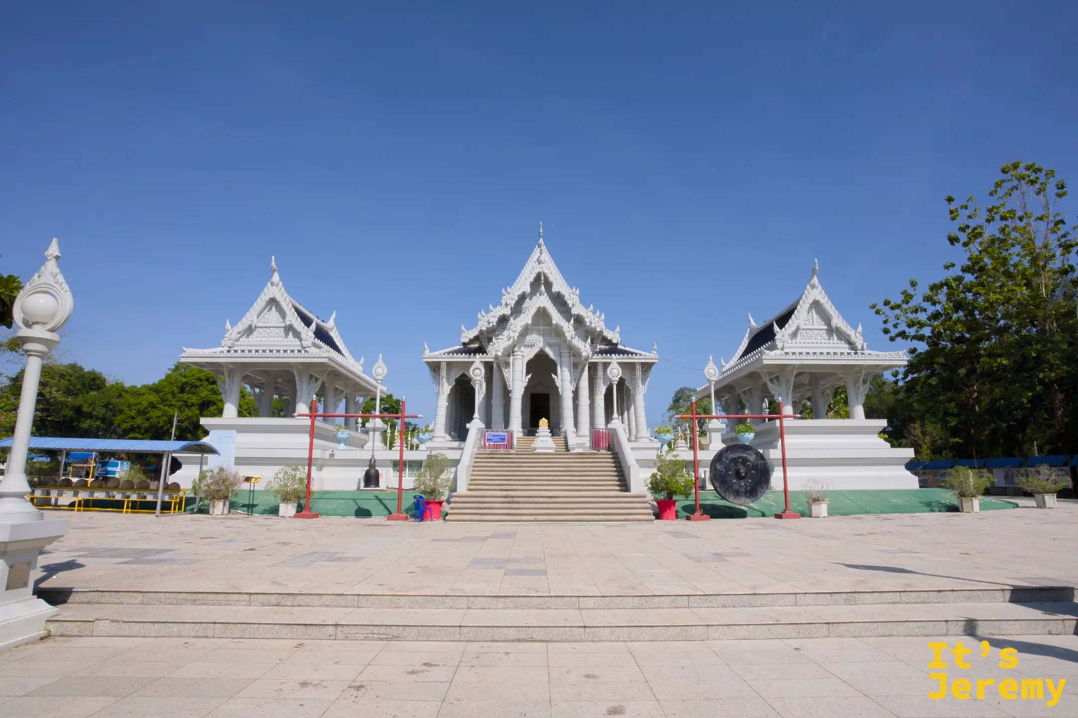 Wat Kaew Korawaram 主殿全景,三棟白殿對稱並排,前方立有銅鐘與橘紅色鐘架