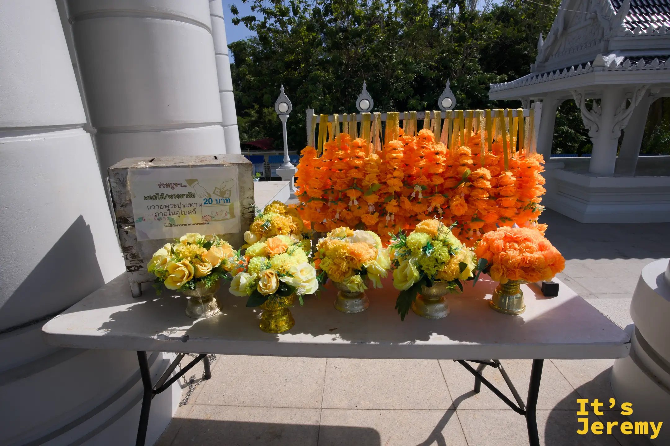 大殿廊柱旁的花環供品桌,橘色萬壽菊花環與黃色玫瑰供花,20 泰銖一串