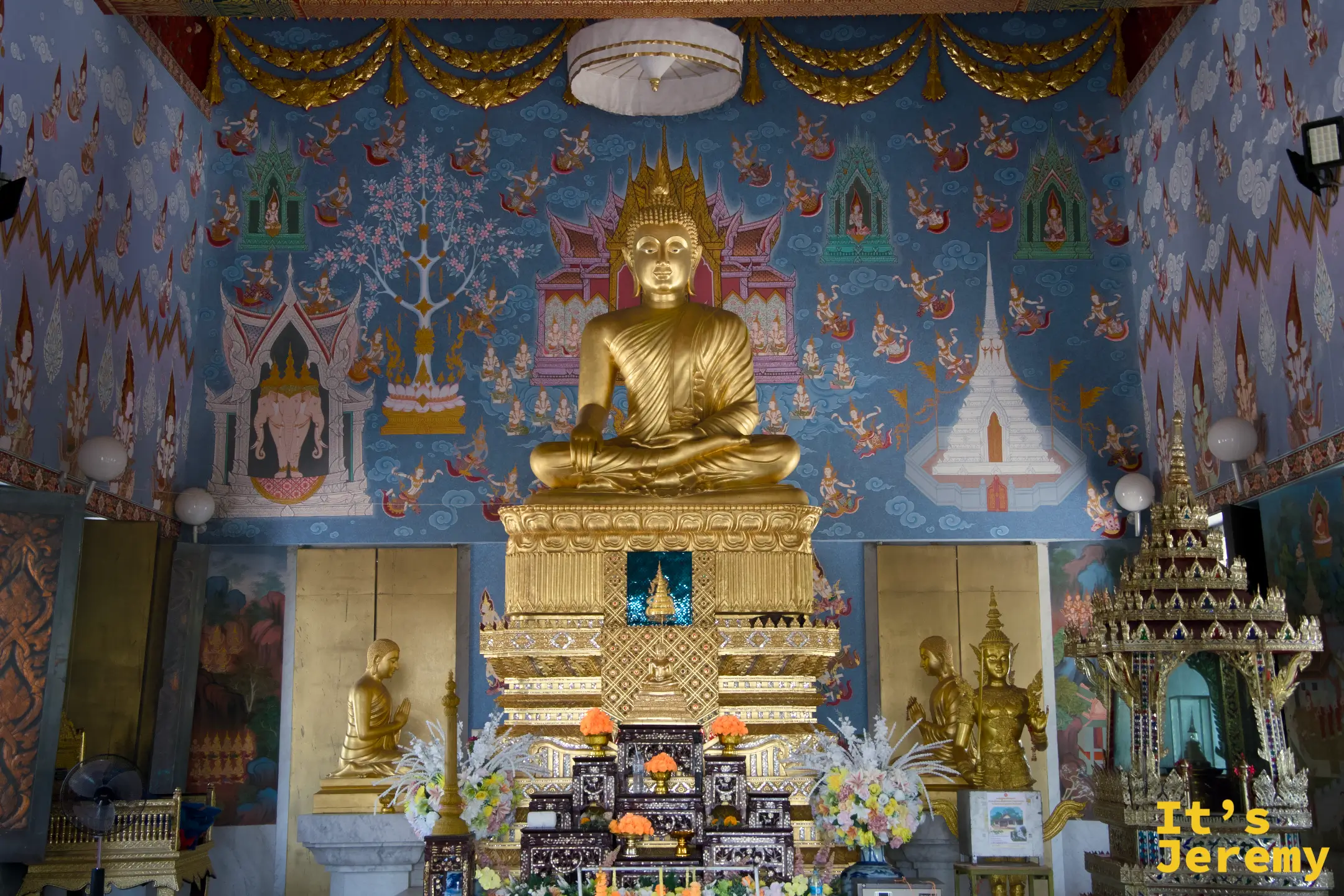 主殿全景,金色主佛與藍底壁畫,佛台兩側可見立像,花束鮮花供奉其前