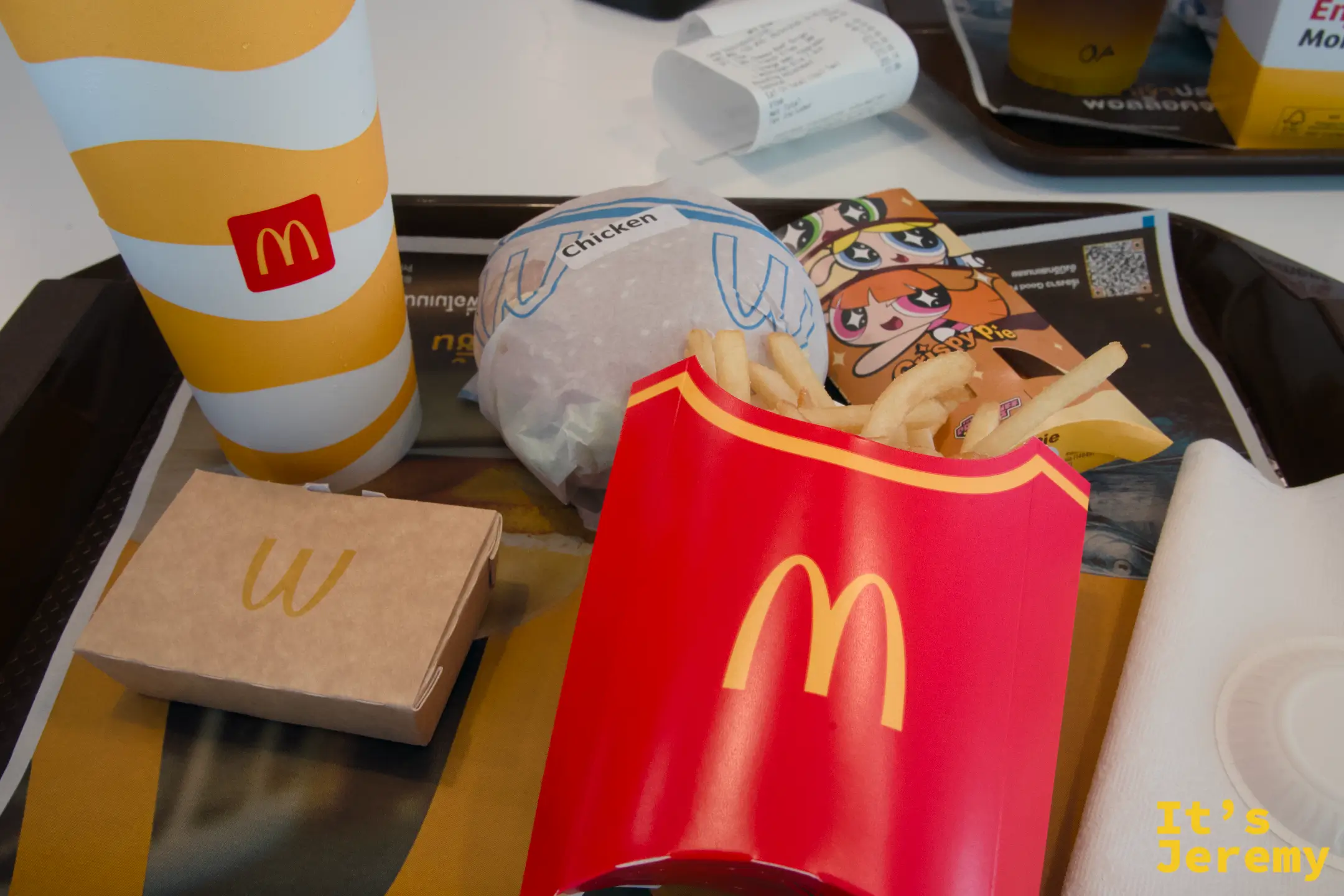 廊曼機場麥當勞桌面,托盤上有 Cheesy Chicken 漢堡、大份薯條、飲料和法式起司菠菜派小盒