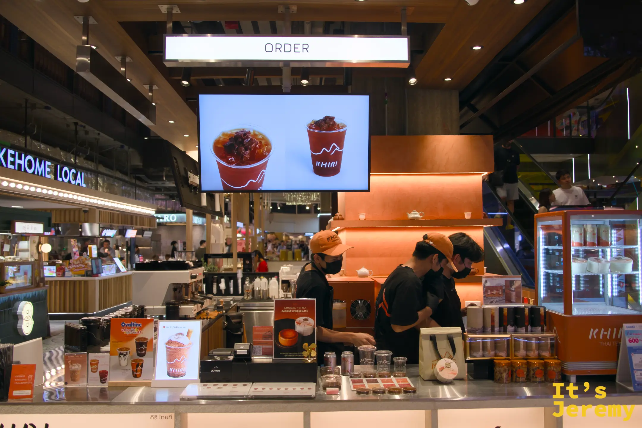 點餐台全景,橘色背牆配上展示螢幕,員工統一黑橘制服