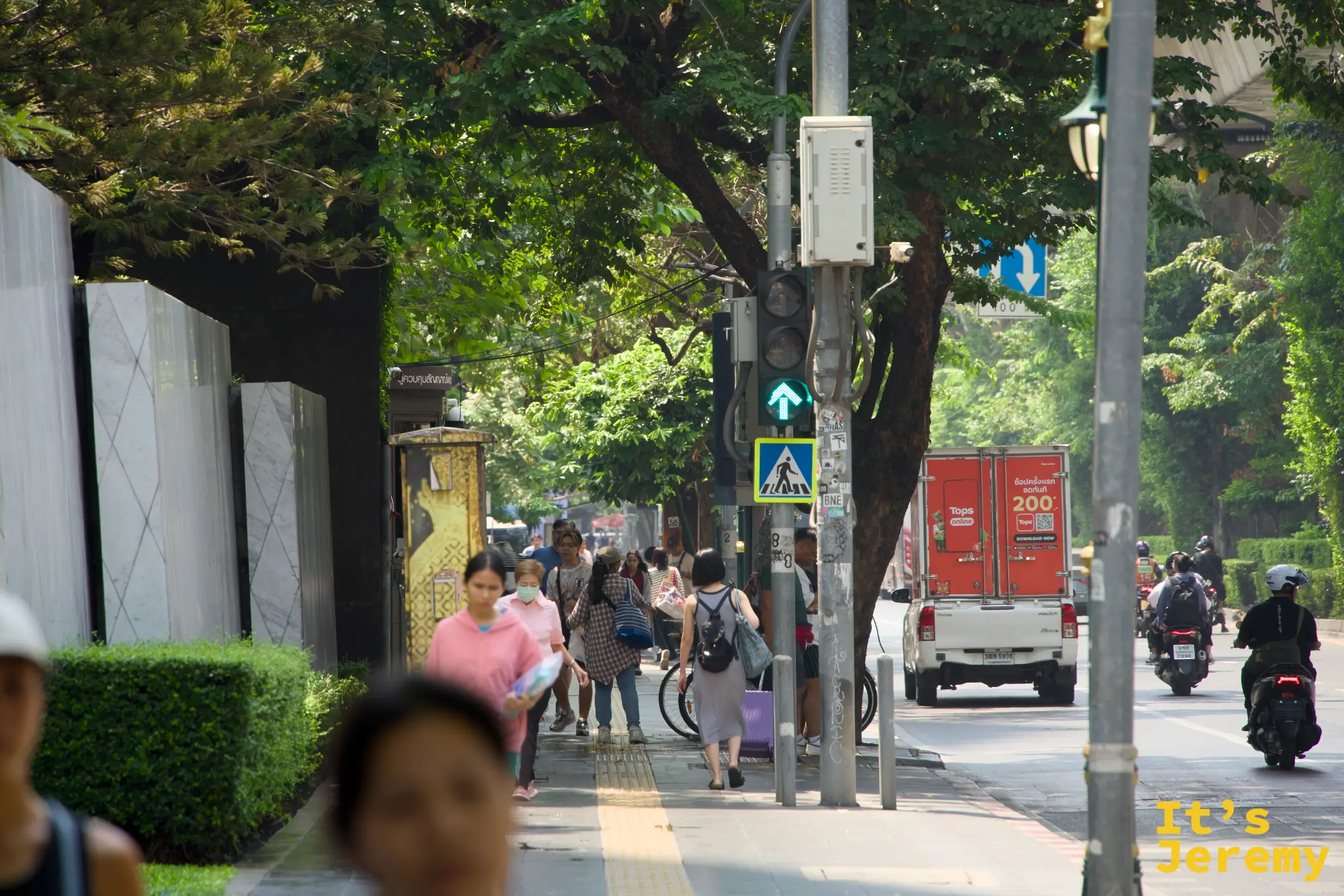 早上的蘇坤蔚路面,行人在有樹蔭的騎樓下走動,遠處是對向車流