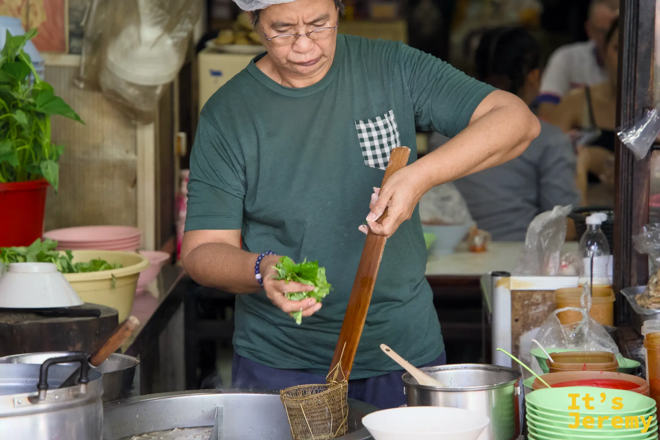 廚師手持長木柄鍋勺,在鍋前燙菜備料,背景是大型湯鍋與整排碗碟