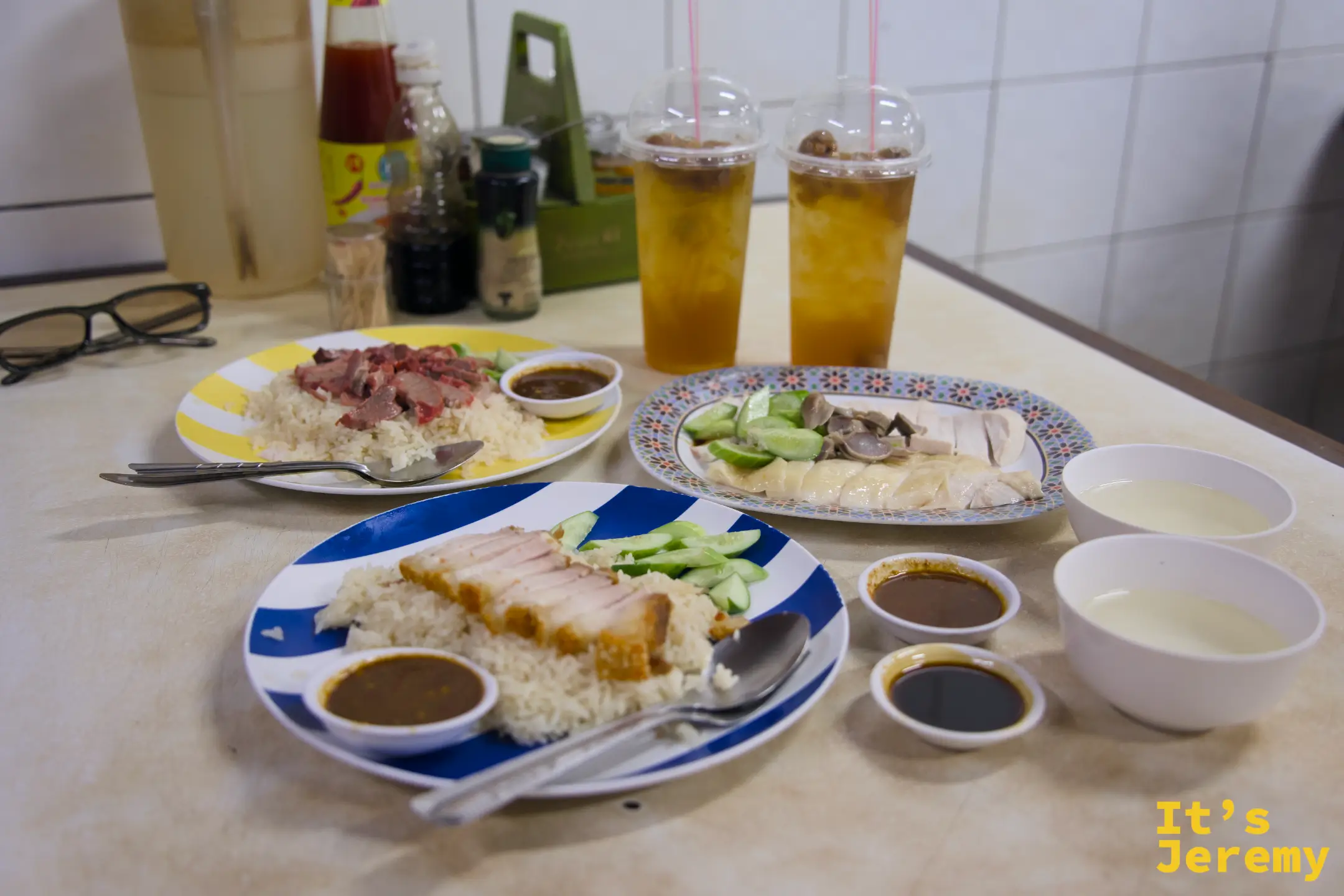 三款配飯正面視角:脆皮豬在前,紅燒肉與白斬雞在後,各附小黃瓜與醬汁,兩杯冰飲並排