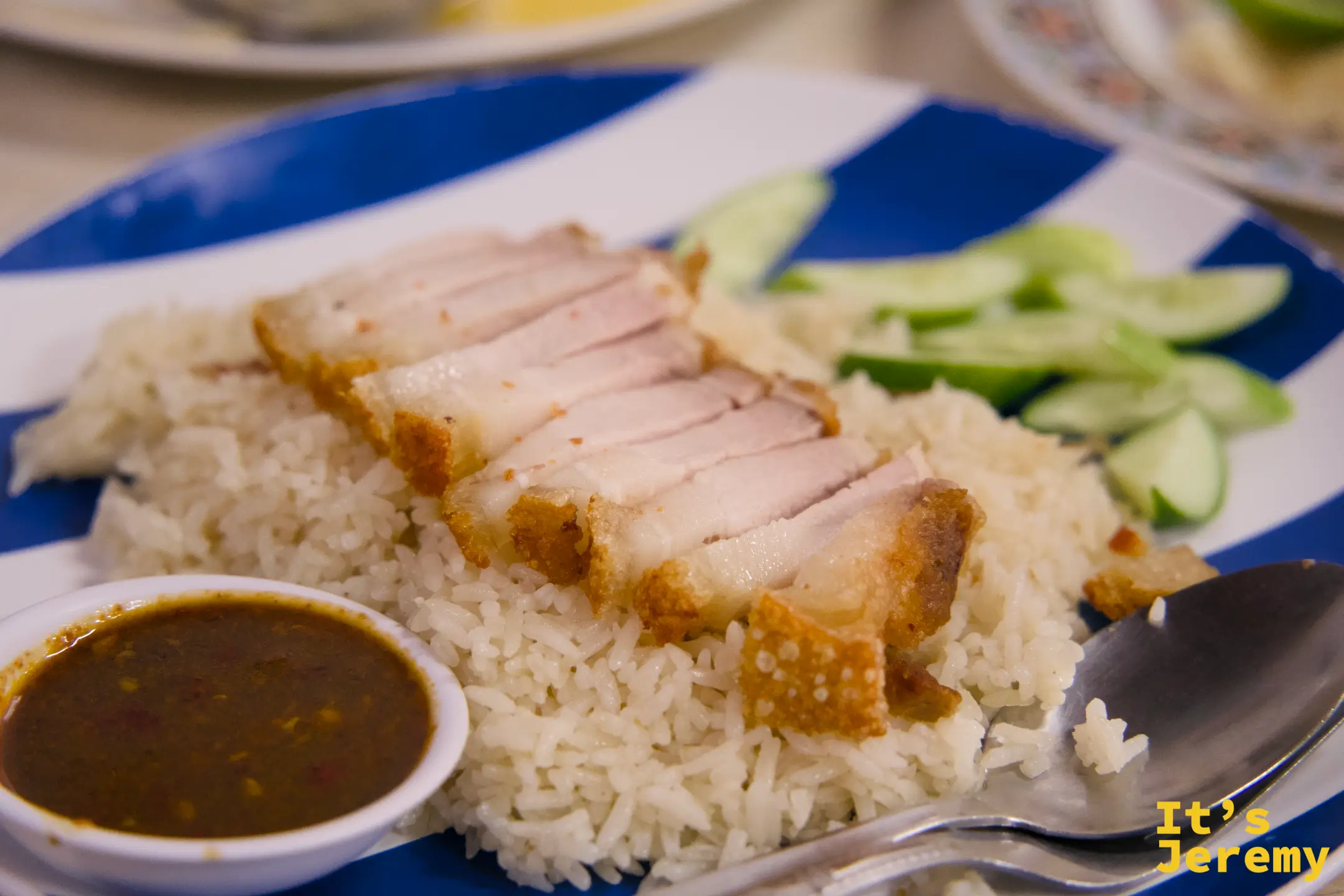 脆皮豬飯特寫:豬皮焦金酥脆,切片整齊鋪在雞油飯上,旁附深紅辣醬,藍白條紋盤