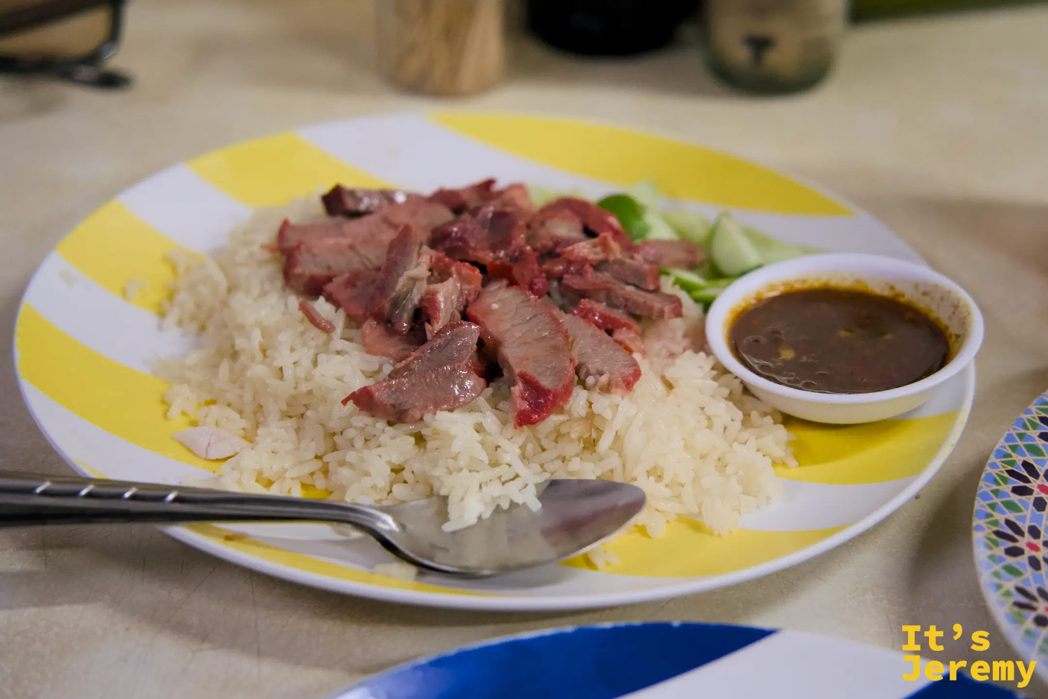 紅燒肉飯特寫:深紅色燒肉切片,鋪在雞油白飯上,旁附深色滷汁醬,黃白條紋盤