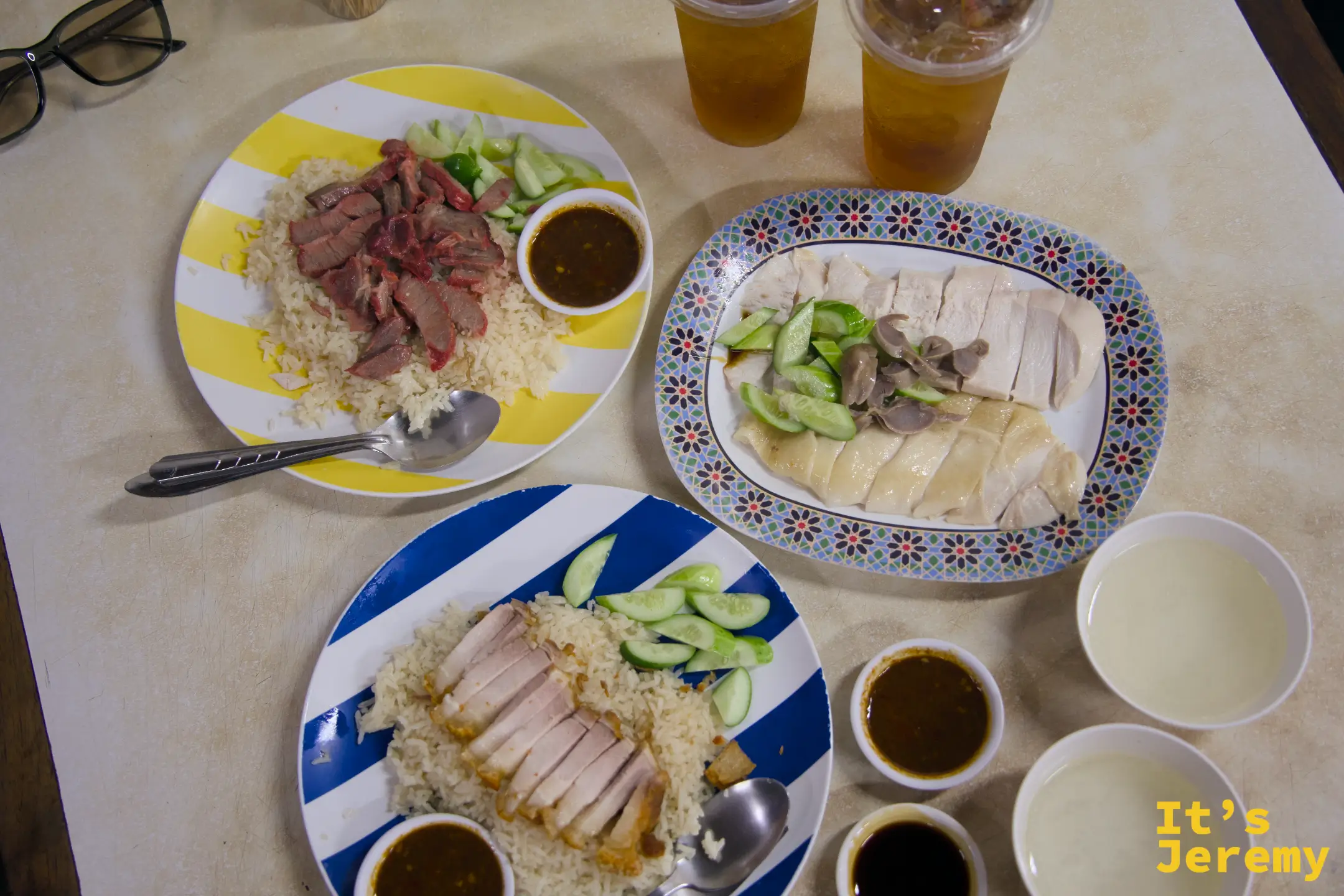 三款配飯全桌:白斬雞、脆皮豬、紅燒肉,各附醬汁與小黃瓜,加上兩杯冰飲,俯瞰全景