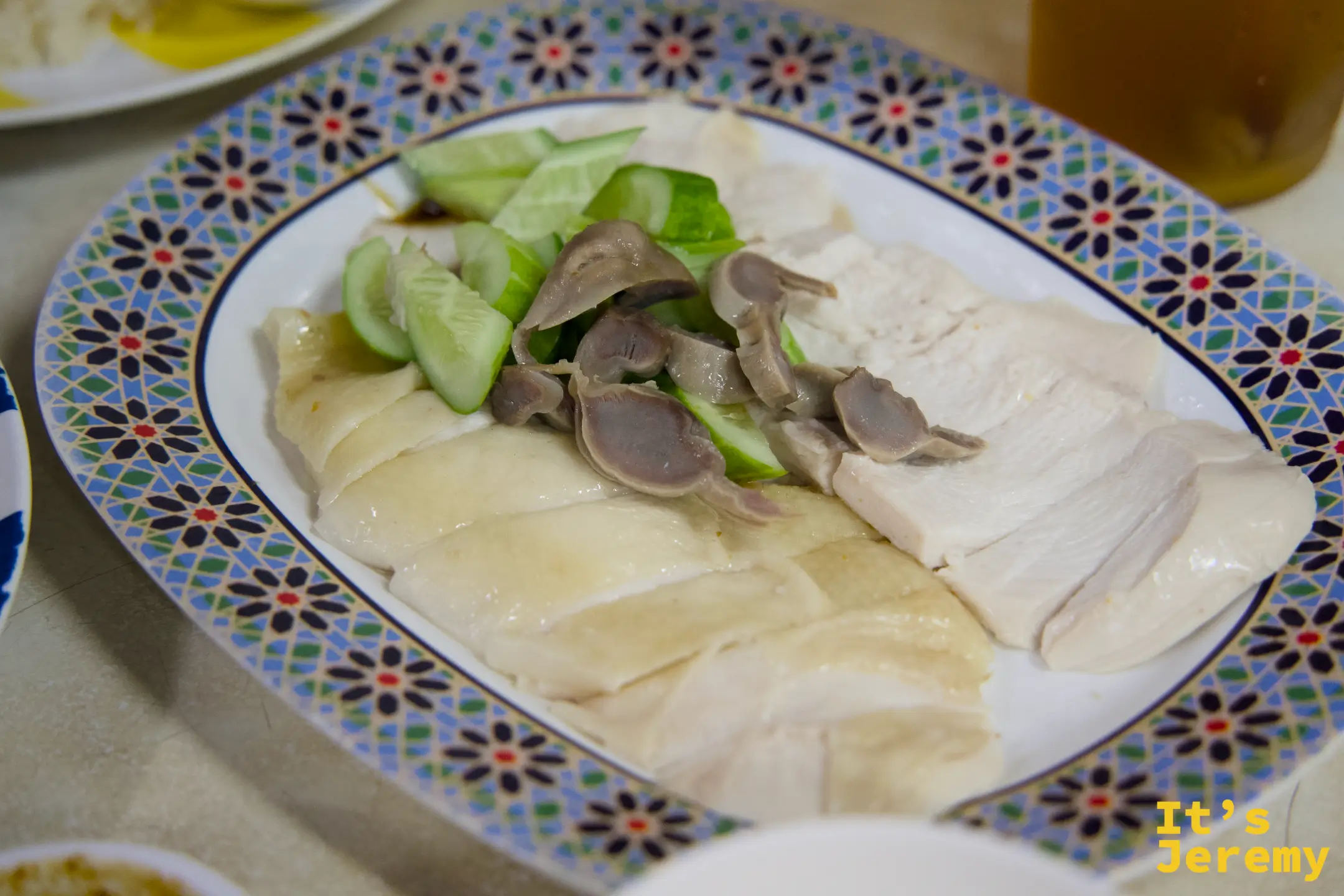 白斬雞飯特寫:嫩滑雞肉切片整齊排列,搭配雞胗與小黃瓜,擺在花紋磁盤上
