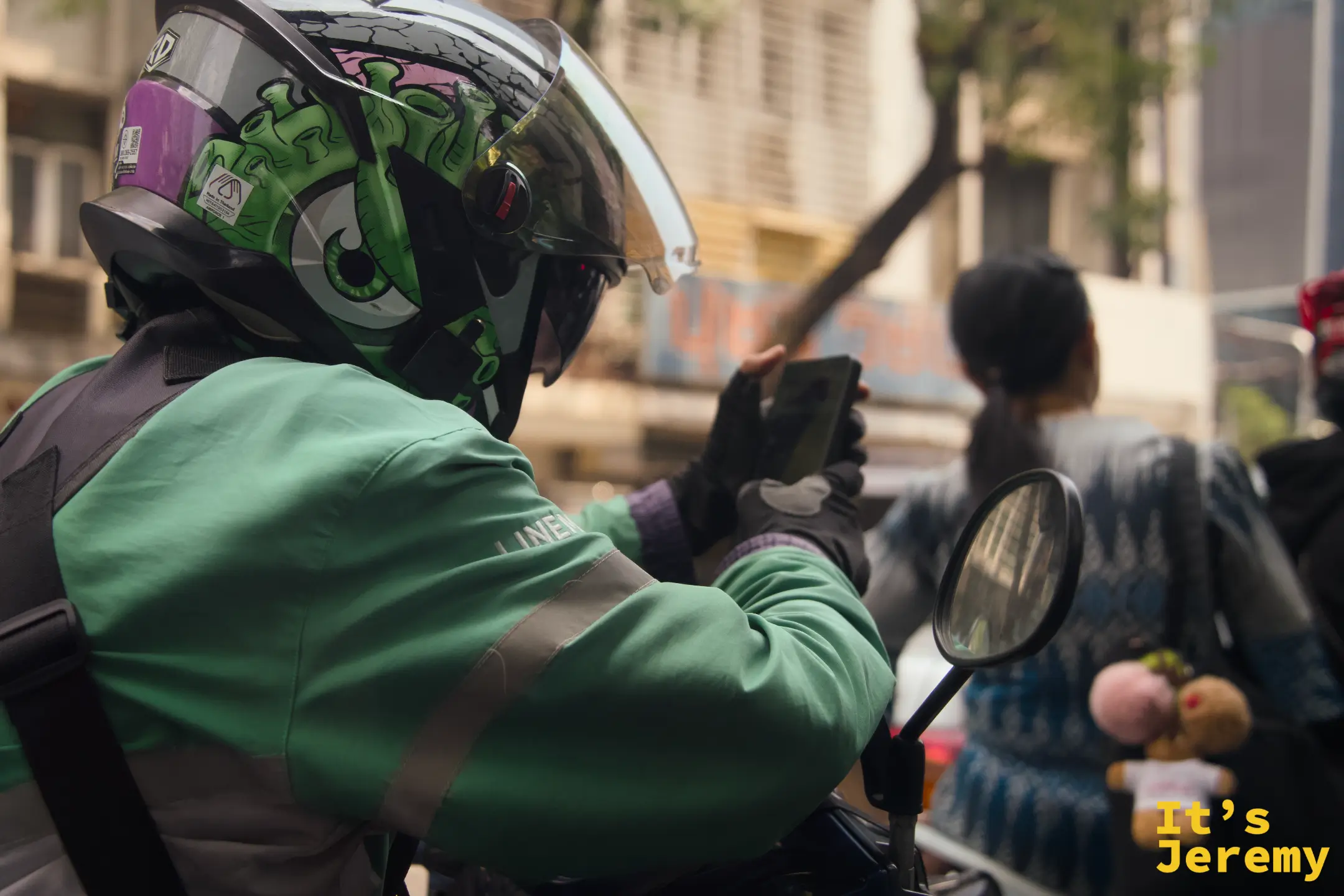 一位 Grab 外送員停紅燈時低頭滑手機,頭盔上的怪獸圖案讓人印象深刻,紅燈滑手機這件事看來不分國籍
