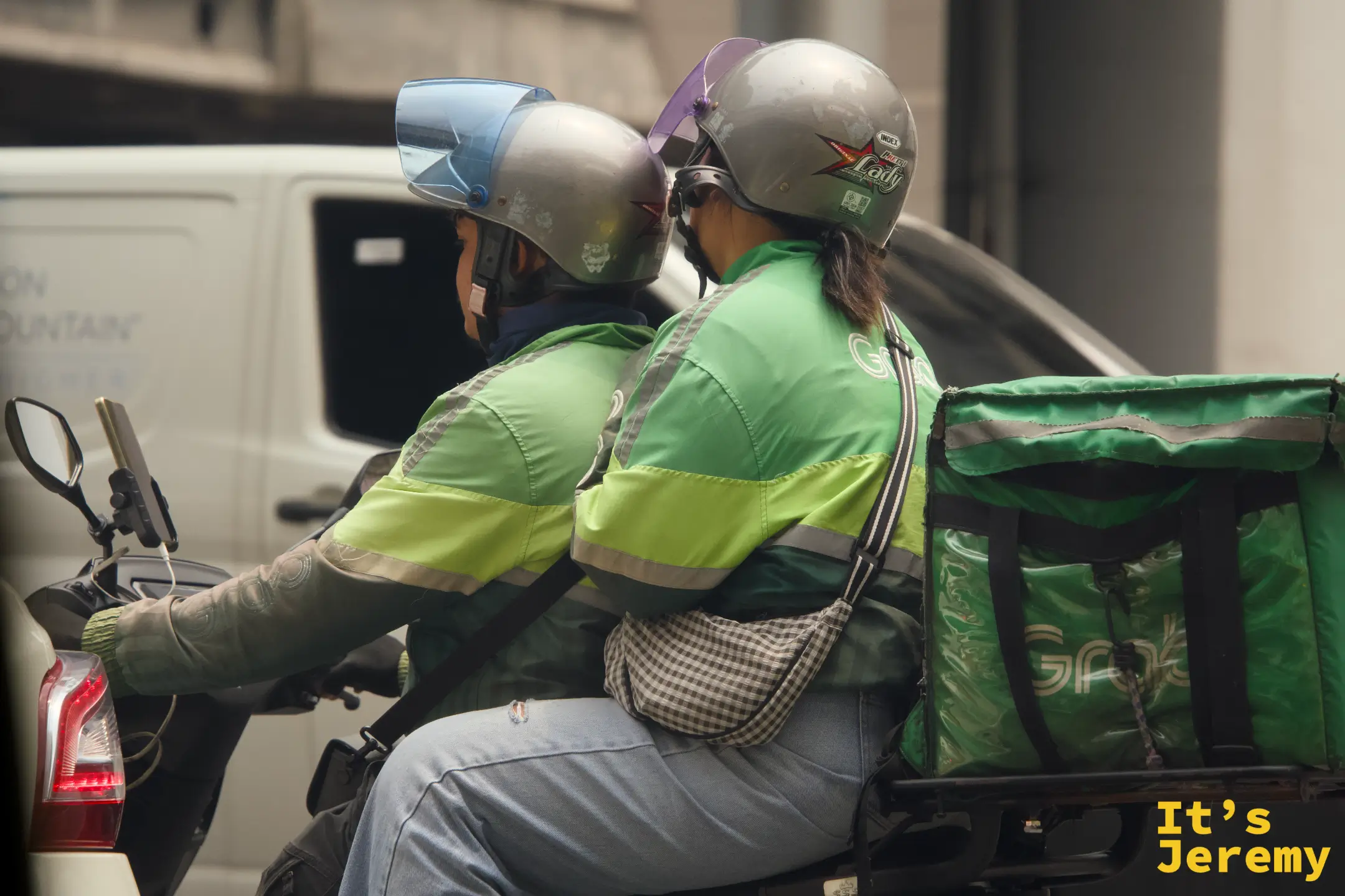 兩位 Grab 外送員共乘一輛機車,後座的人揹著外送保溫箱,像是正要出任務的搭檔
