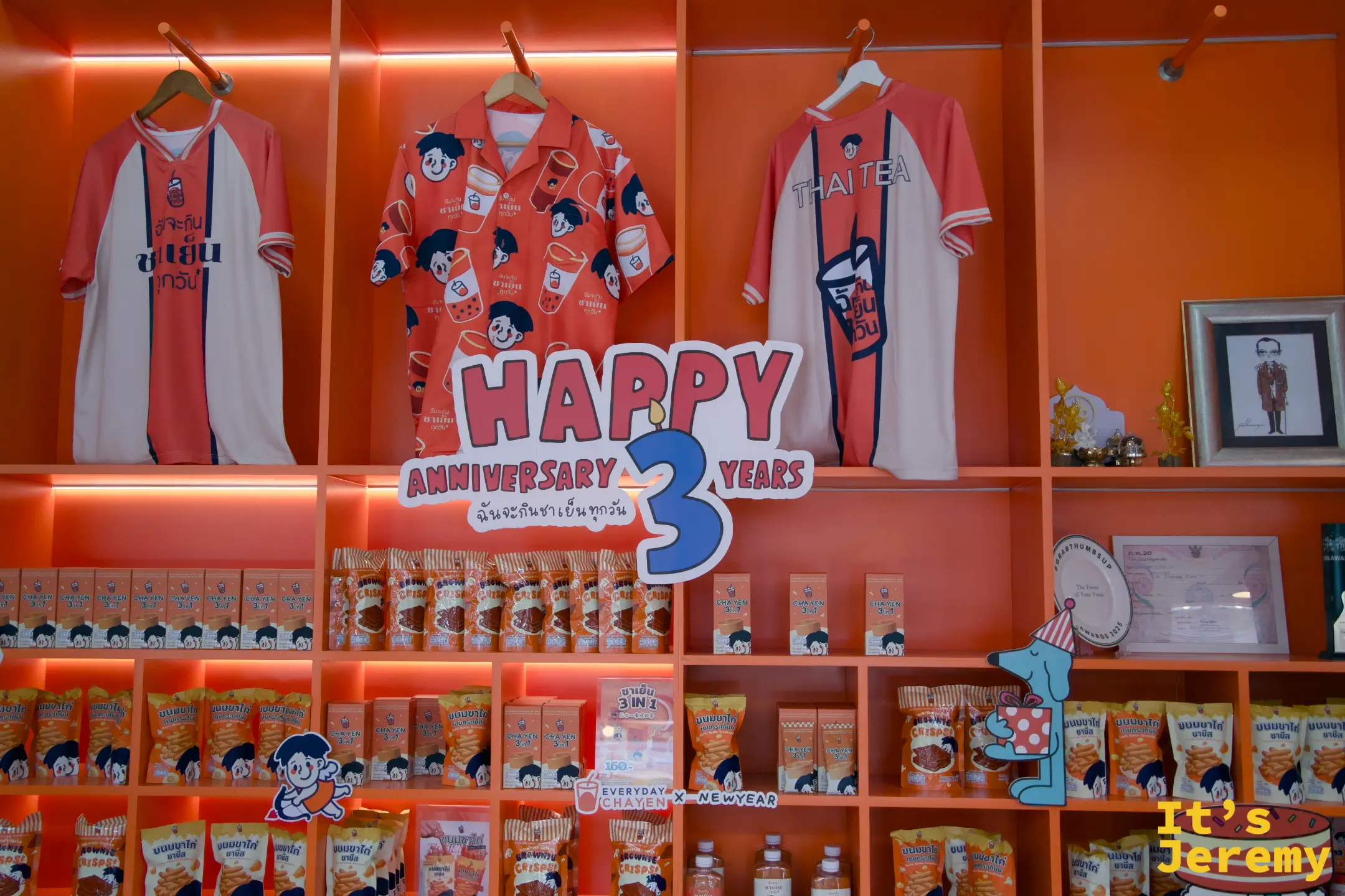 品牌展示架：Thai Tea 印花 polo 衫與運動衫，下方擺滿聯名零食包，Happy 3 Years Anniversary 立體字居中