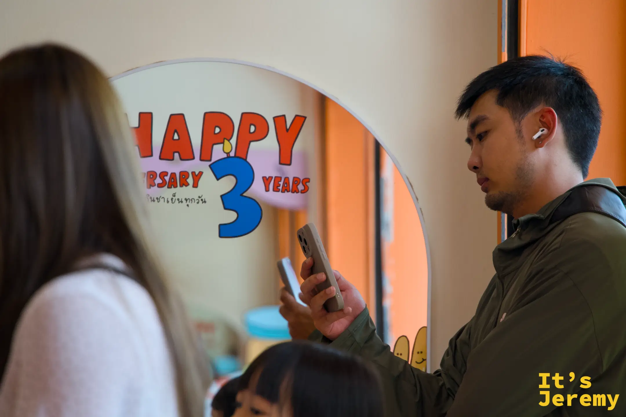 顧客手持手機在 Happy Anniversary 3 Years 拱形鏡前拍照，前景為另一位顧客的背影
