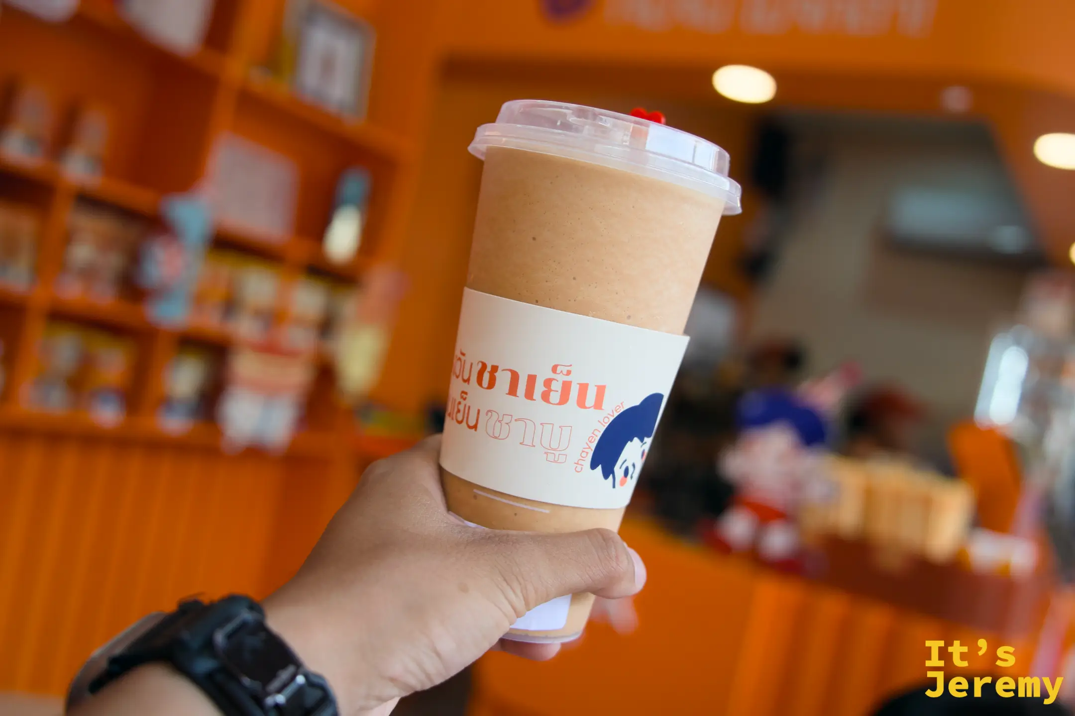 手持 Everyday Thai Tea 品牌杯,橘色杯身在陽光下顯色飽和,BTS 站出口的陽光從背後打進來
