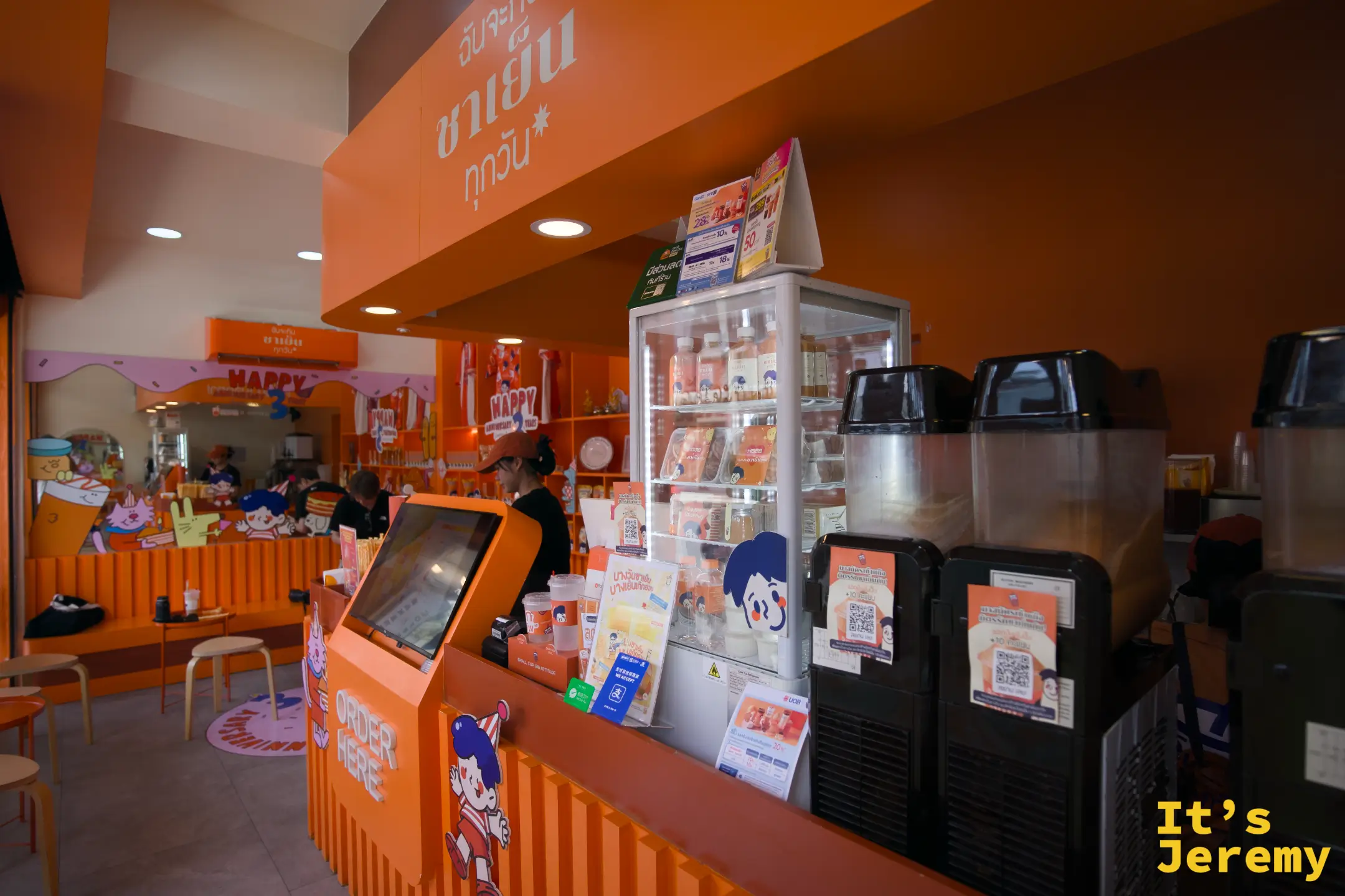店內點餐機台與冷藏展示冰箱，右側為製茶區，整體採全橘色設計