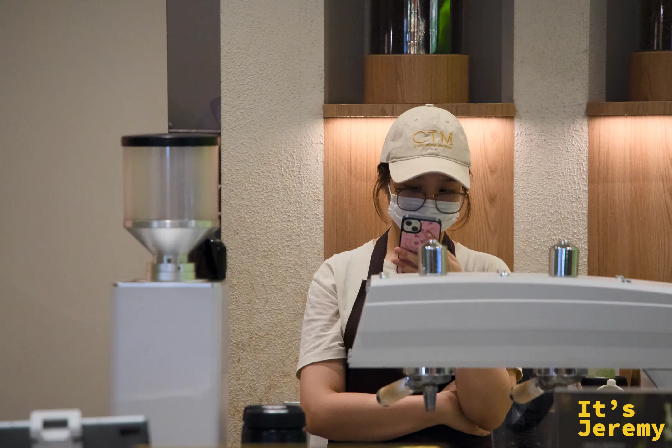 女性店員空檔低頭滑手機，espresso 機與磨豆機在旁待命