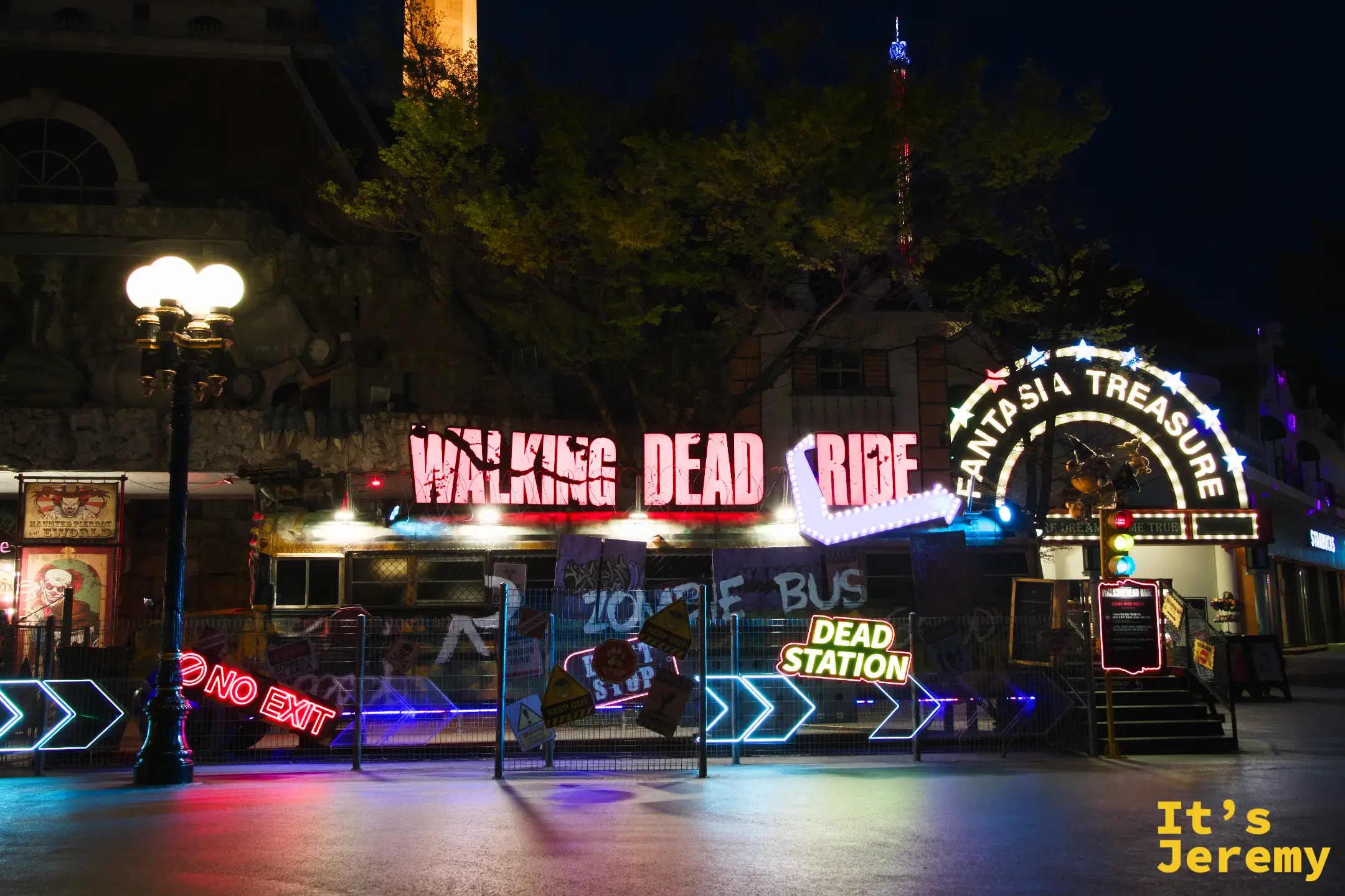 Walking Dead Ride 主題區的紅色霓虹招牌，右側有「FANTASIA TREASURE」拱門，地面散落「NO EXIT」、「DEAD STATION」霓虹道具，左邊是一盞歐式雙球路燈