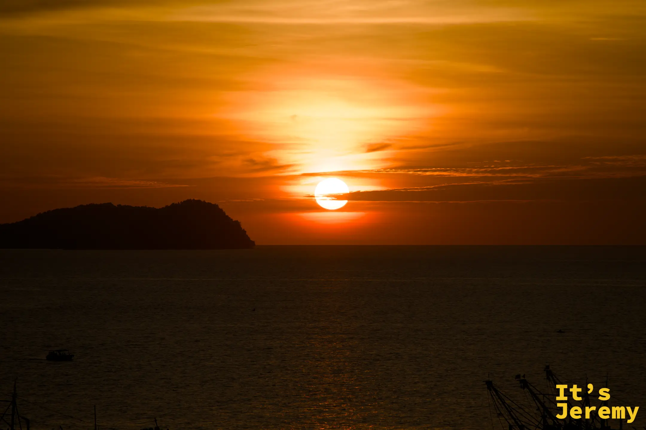 亞庇日落，深橘紅色天空，太陽貼近加雅島輪廓，漁船靜泊港中