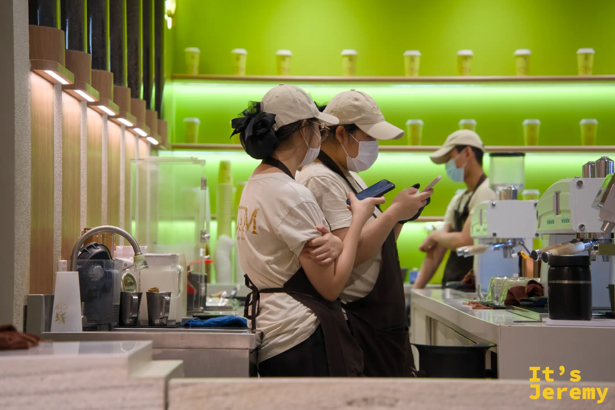 兩位女性店員並排滑手機，右側另一位正在備料