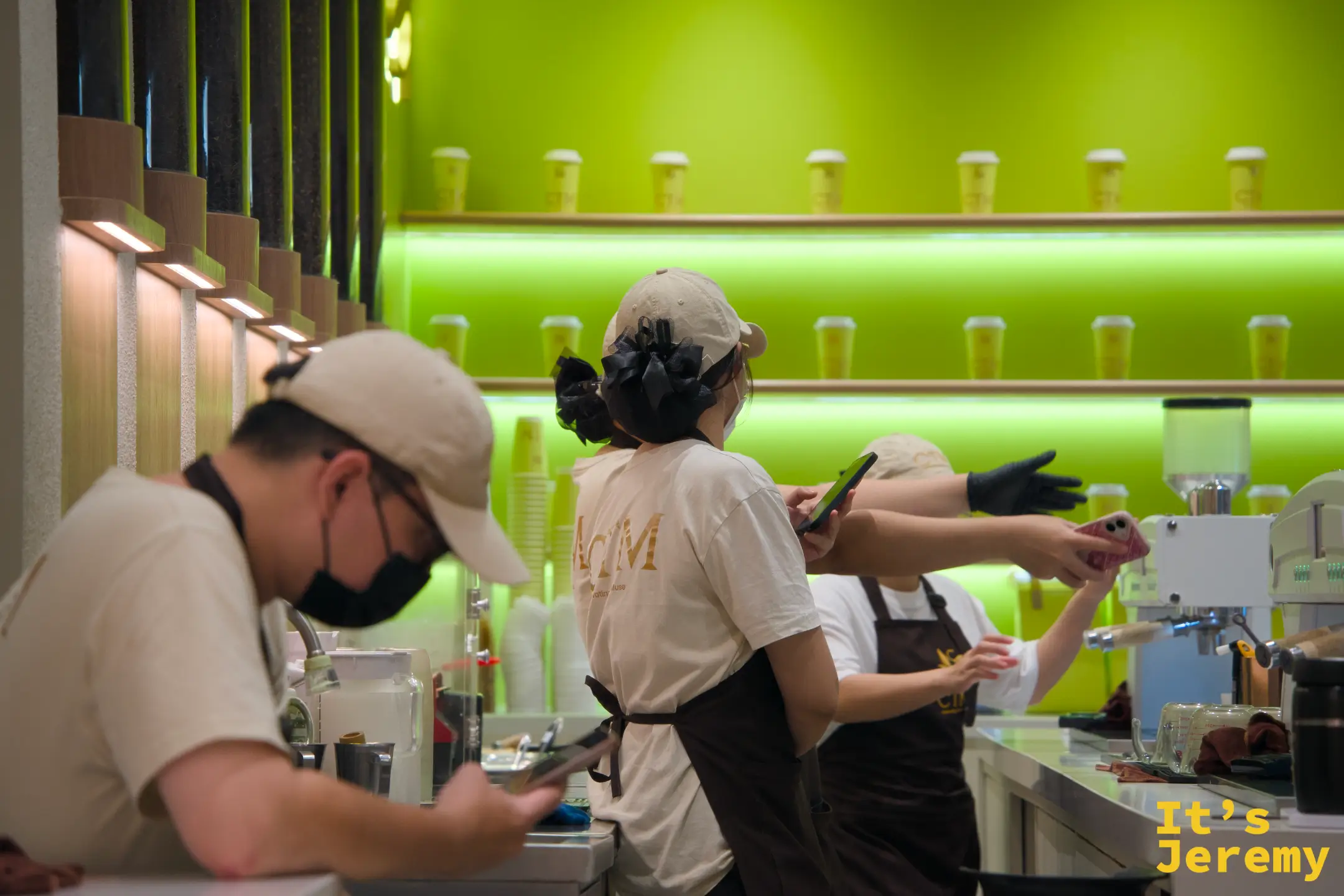 前方男性店員低頭滑手機，後方兩位店員似乎在聊天