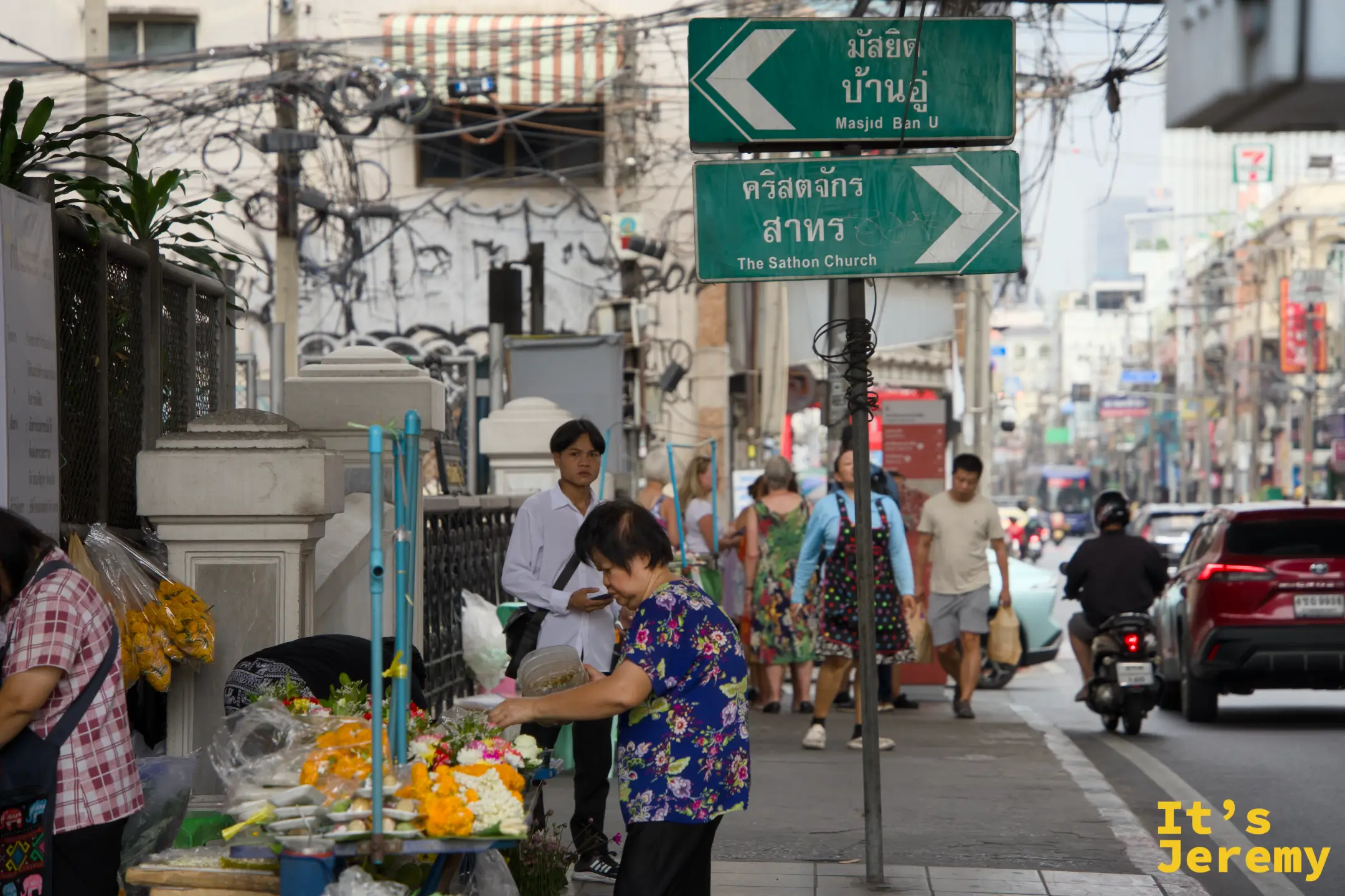 石龍軍路路口,綠色英文路標指向 Masjid Ban U 和 The Sathon Church,前景有花攤