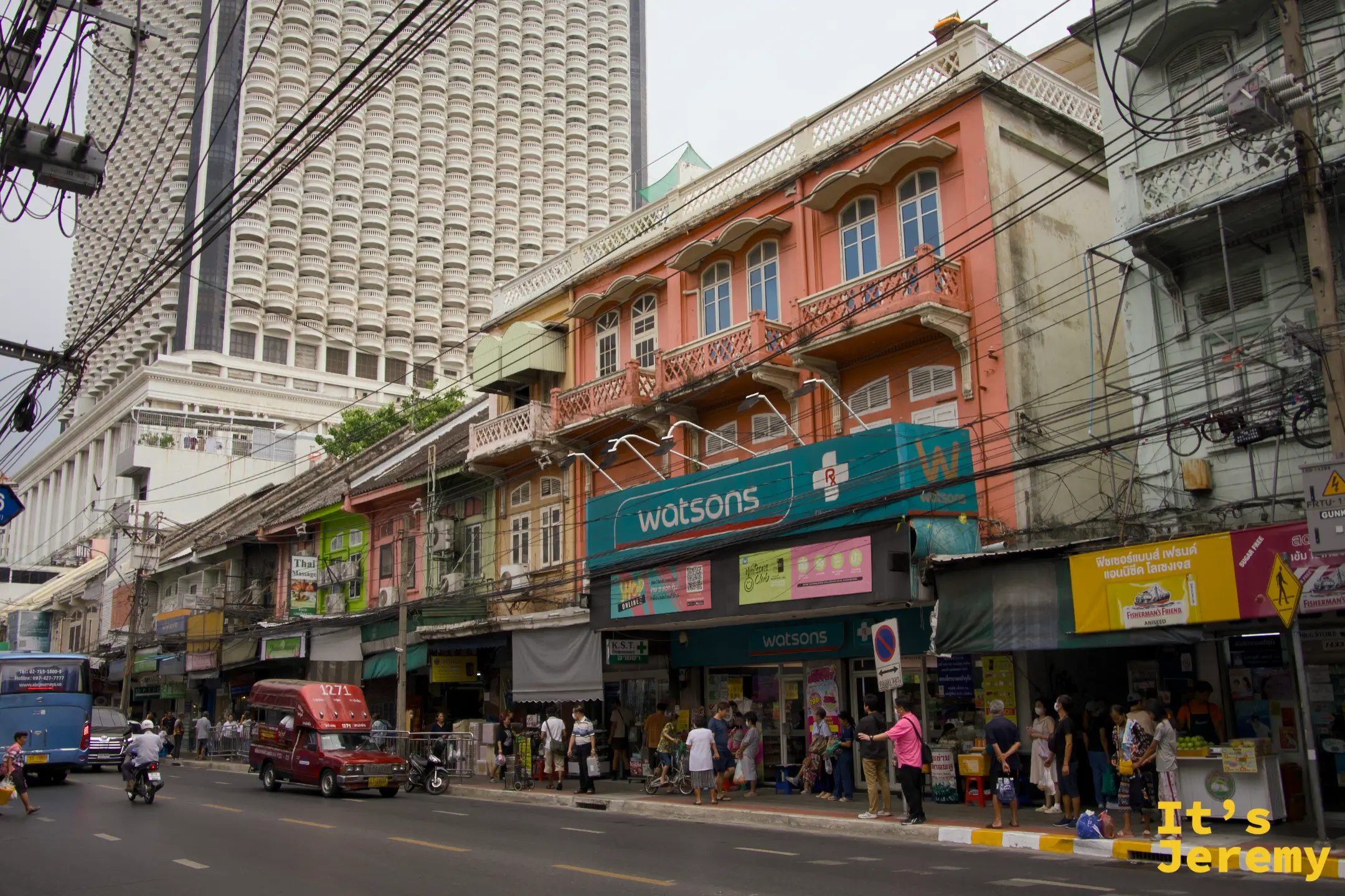 粉紅色兩層老店屋的 Watsons,背後是現代蜂巢格玻璃帷幕高樓,前景紅色嘟嘟車