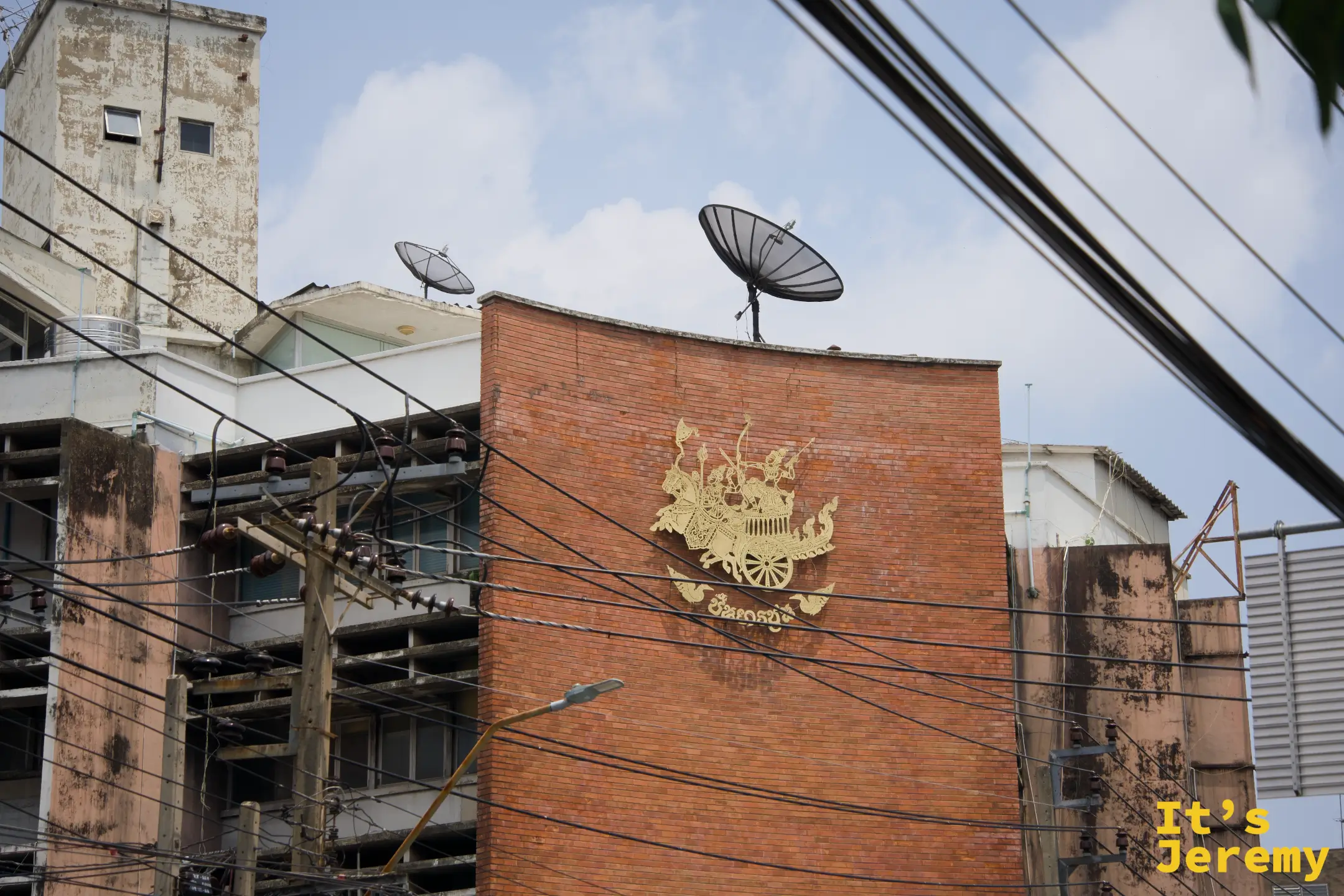 磚造老建築外牆的金色皇家徽章圖騰,背後是衛星天線和廢棄廠房