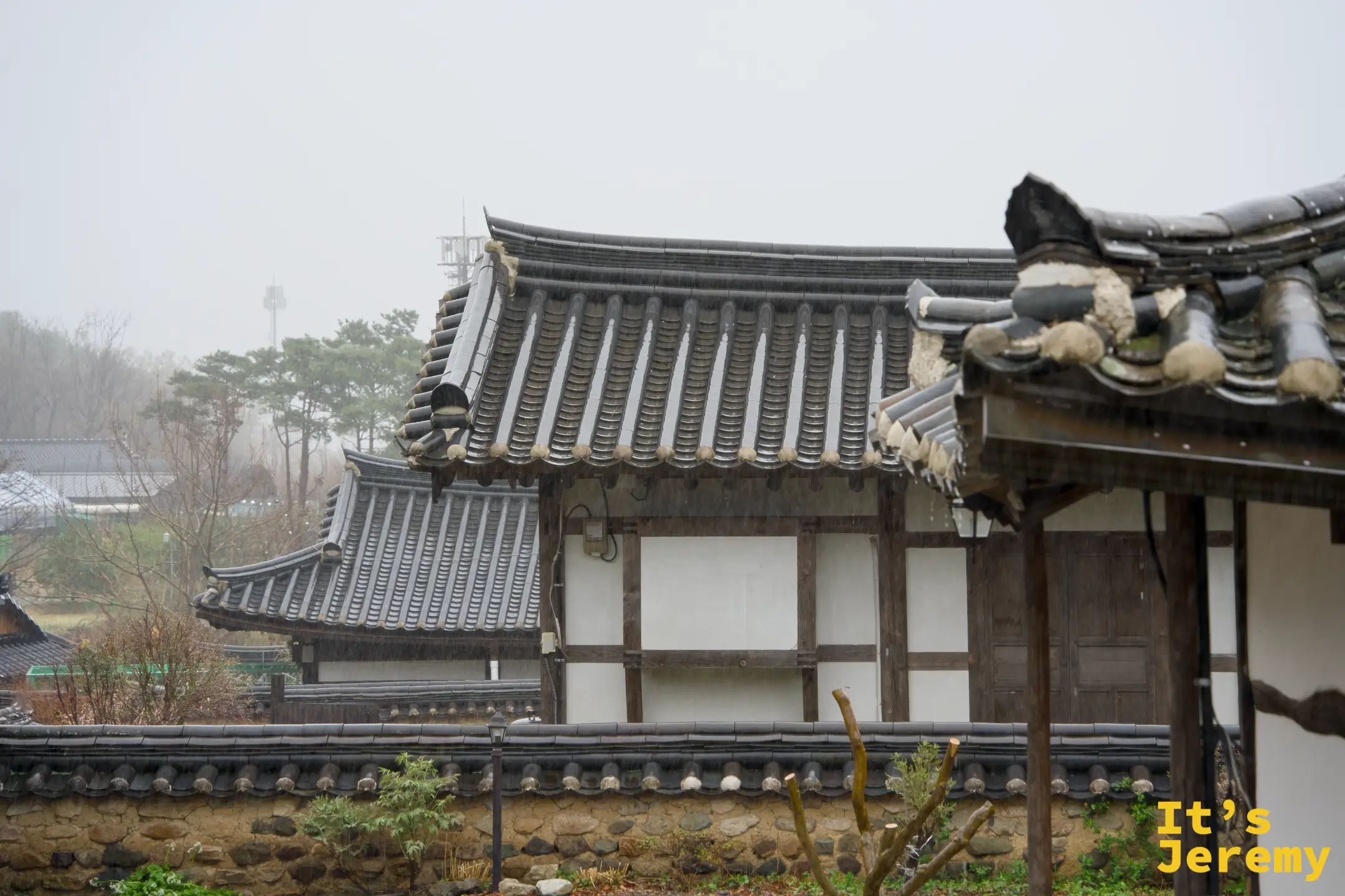 雨霧中疊出層次的韓屋屋頂群，遠方山頭隱入低雲，灰白天空讓瓦片顯得格外沉靜