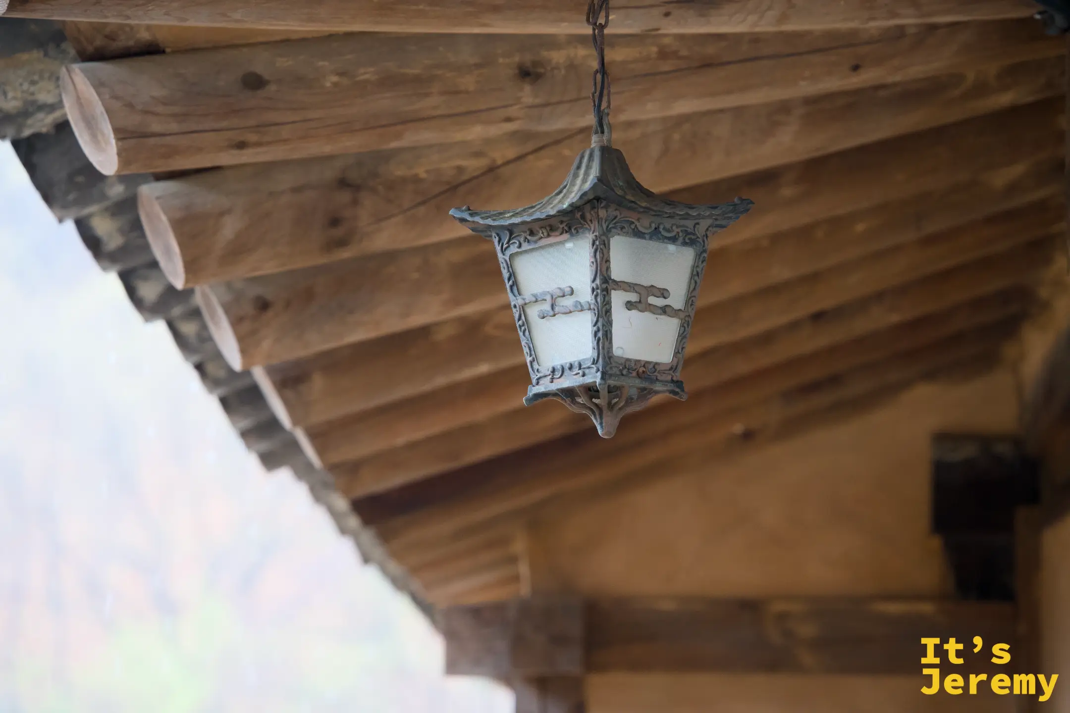 韓屋廊廡下懸掛的傳統宮燈，木紋天花板在雨霧中透著暖意