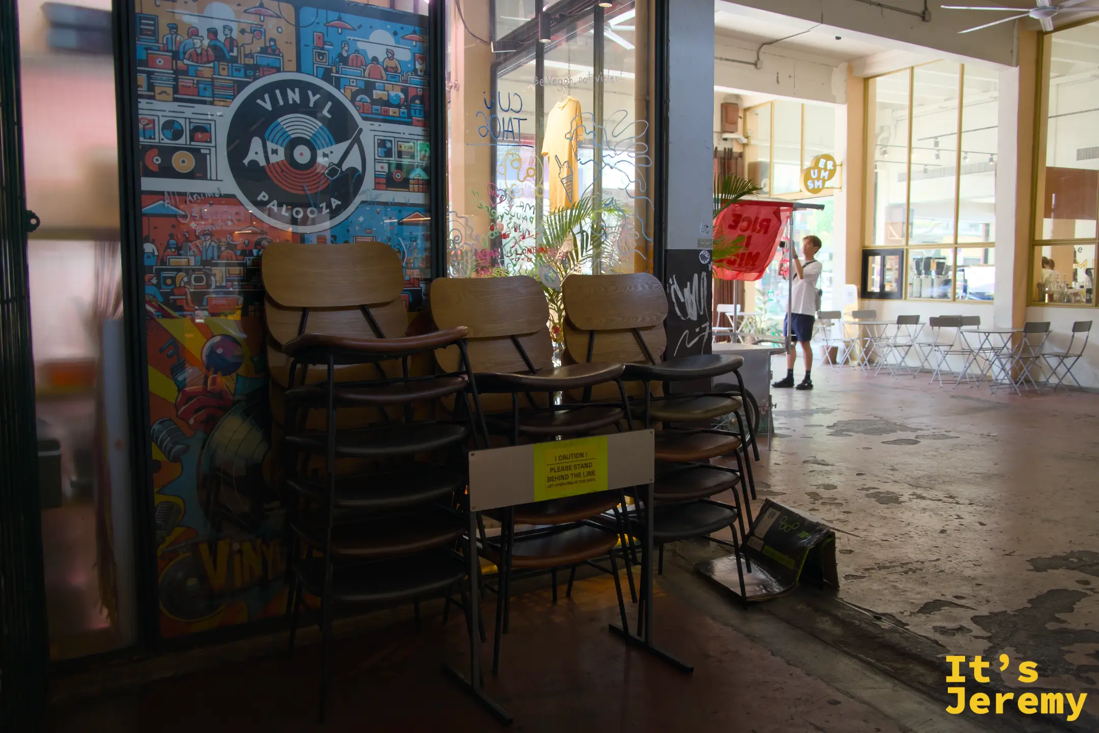 THE WAREHOUSE 一樓:Vinyl Apalooza 唱片市集的插畫海報貼在玻璃門上,前景是堆疊的木椅,空曠的水泥地