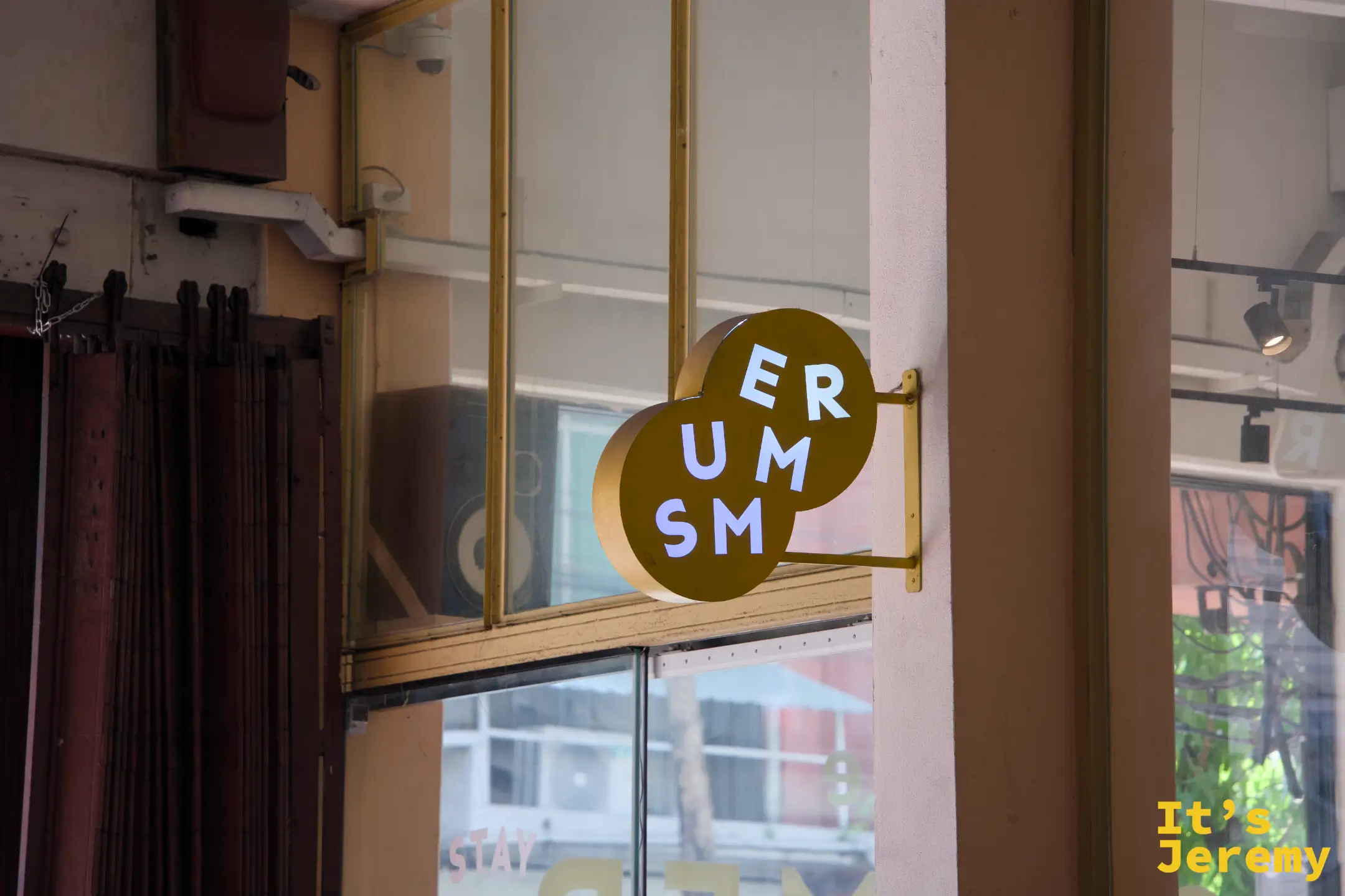 建築外側掛著咖啡色圓形招牌「ER UM SM」,後方玻璃窗內可見大型監聽音箱