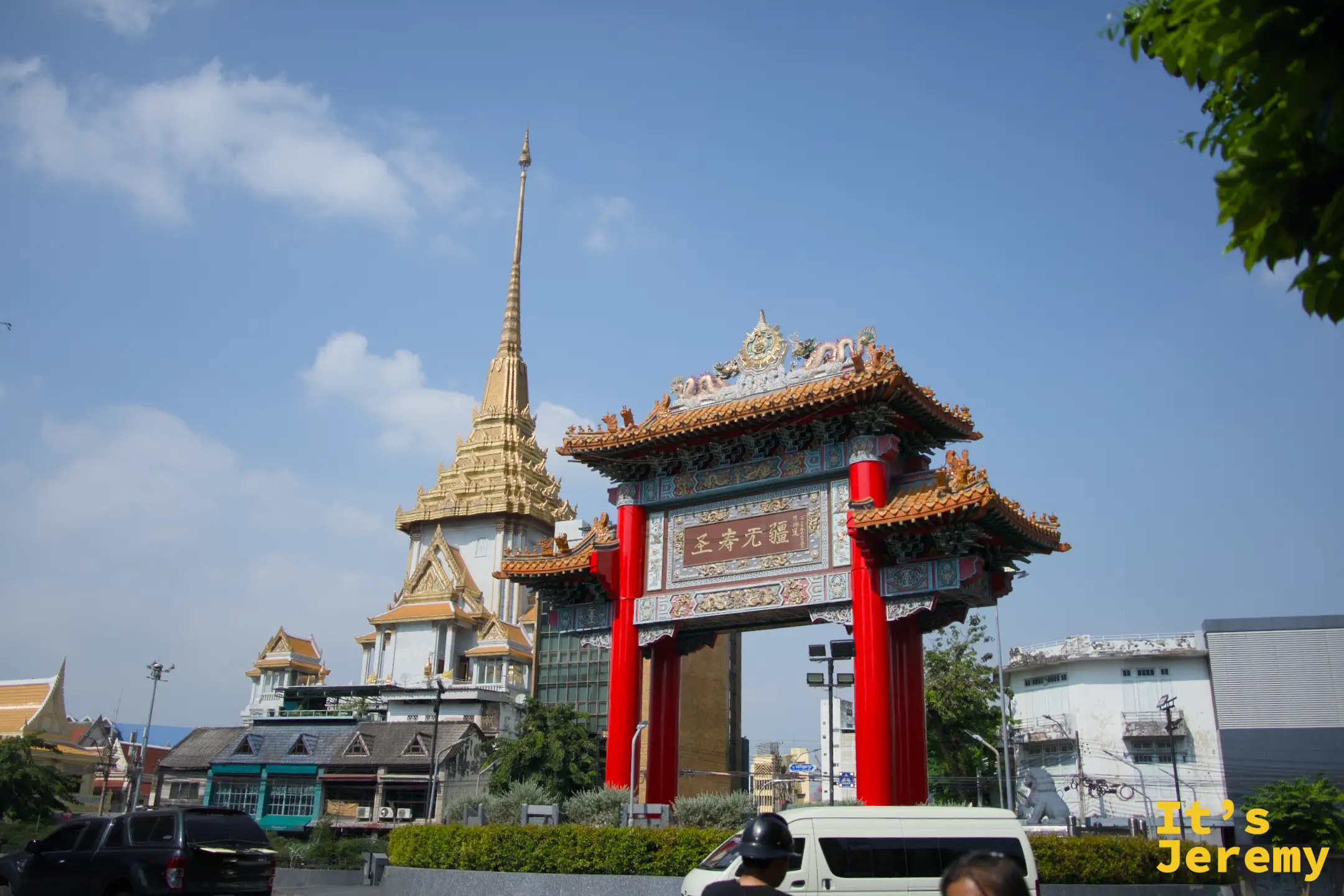 大型中式彩繪牌樓,後方可見 Wat Trimit 金佛寺的金色尖塔,藍天白雲