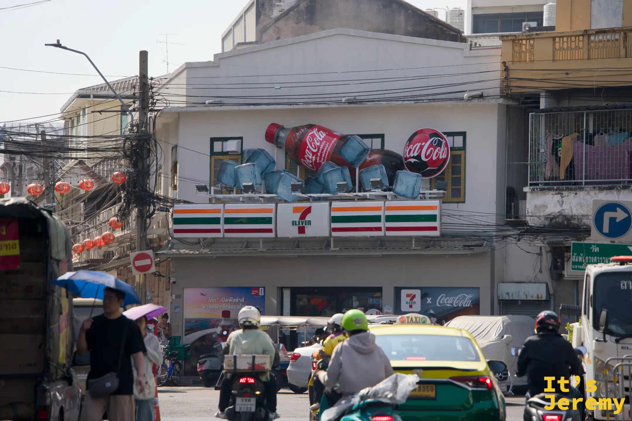 街口 7-Eleven 外牆上方有立體 Coca-Cola 玻璃瓶廣告裝置,前景是交通與行人
