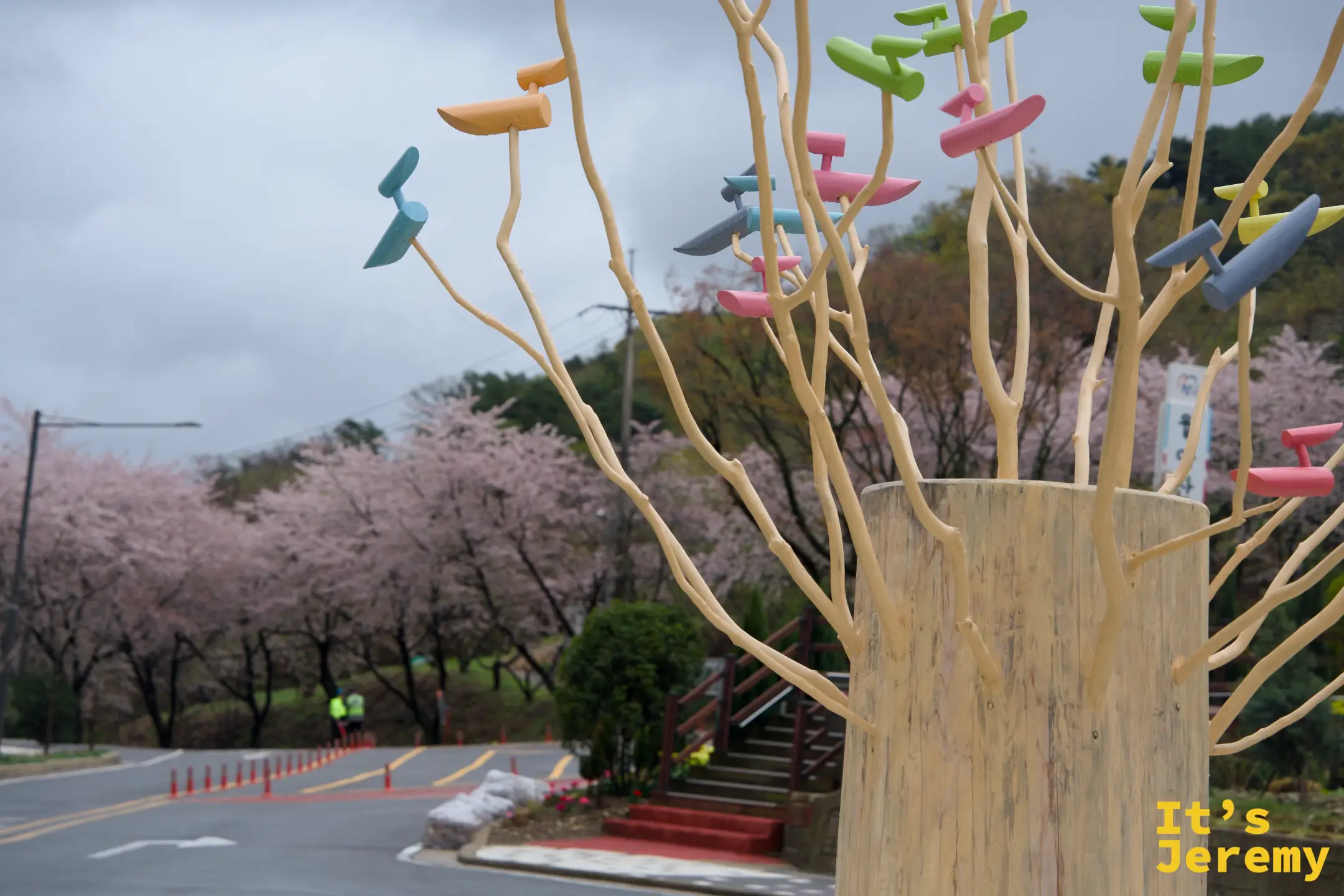月牙山公園入口旁的彩色枝葉藝術裝置，前景鮮豔，背景是霧中的粉色花道