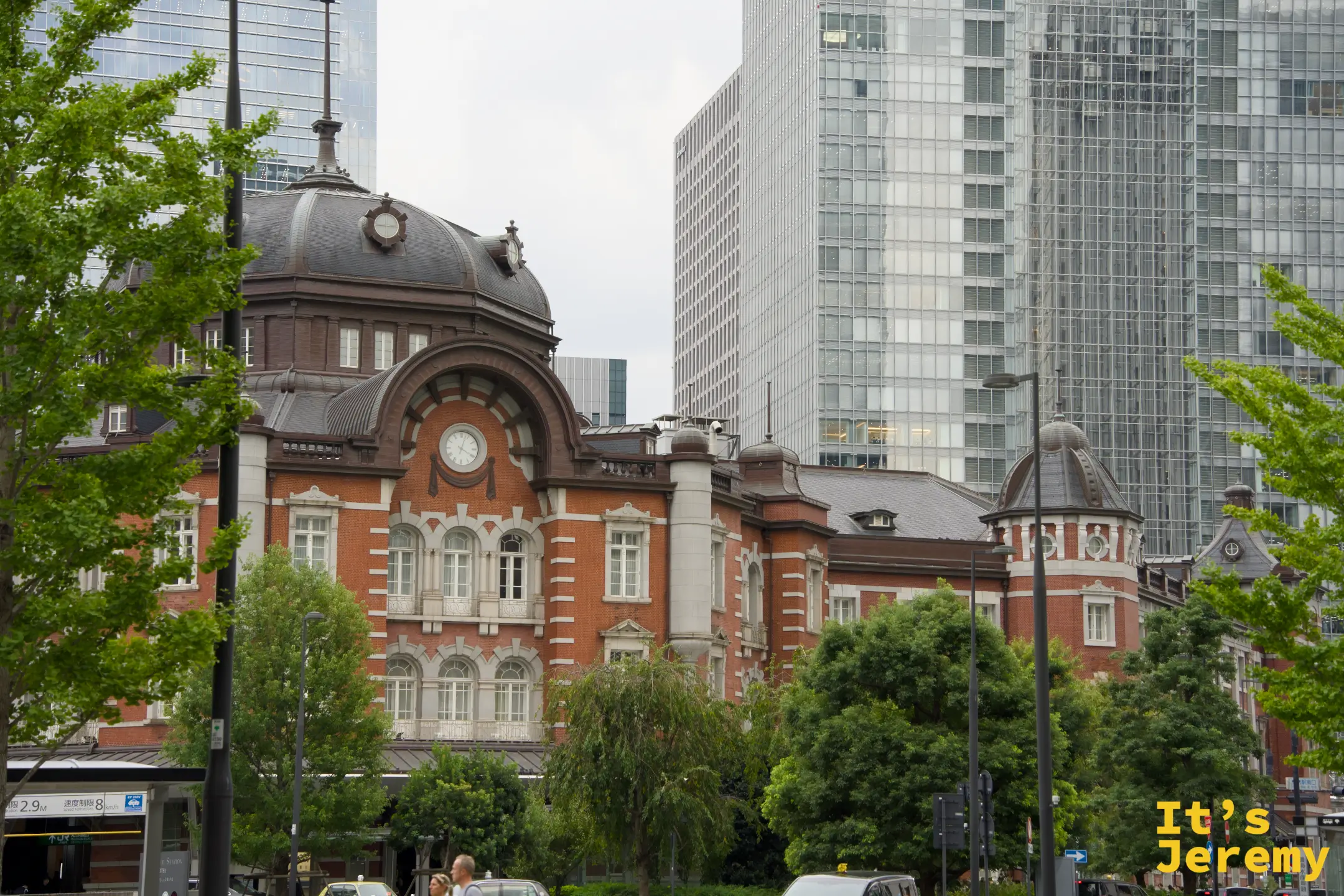 從街道旁樹叢間望向東京車站圓頂，背後是現代辦公大樓