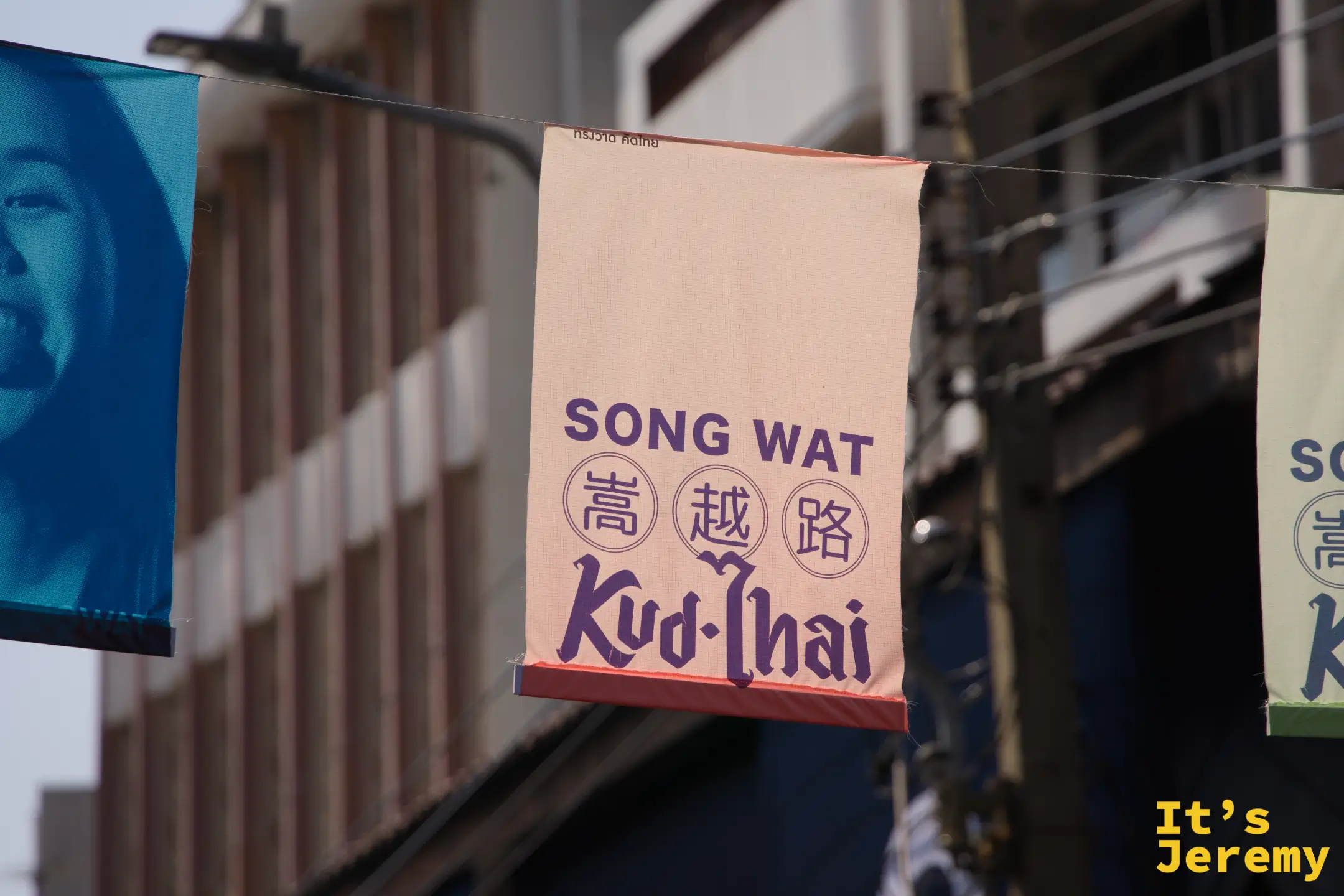 「SONG WAT 嵩越路 Kud-Thai」旗幟近景，粉橘底色搭配深色字體，嵩越路社群品牌的核心視覺
