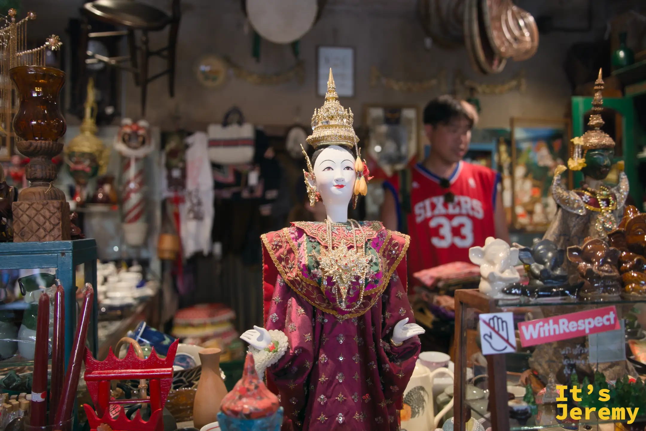 Tang Chae Studio 內的泰國古典舞者人偶，身著金冠與精工刺繡朱紅禮服，背景是古董雜物堆疊