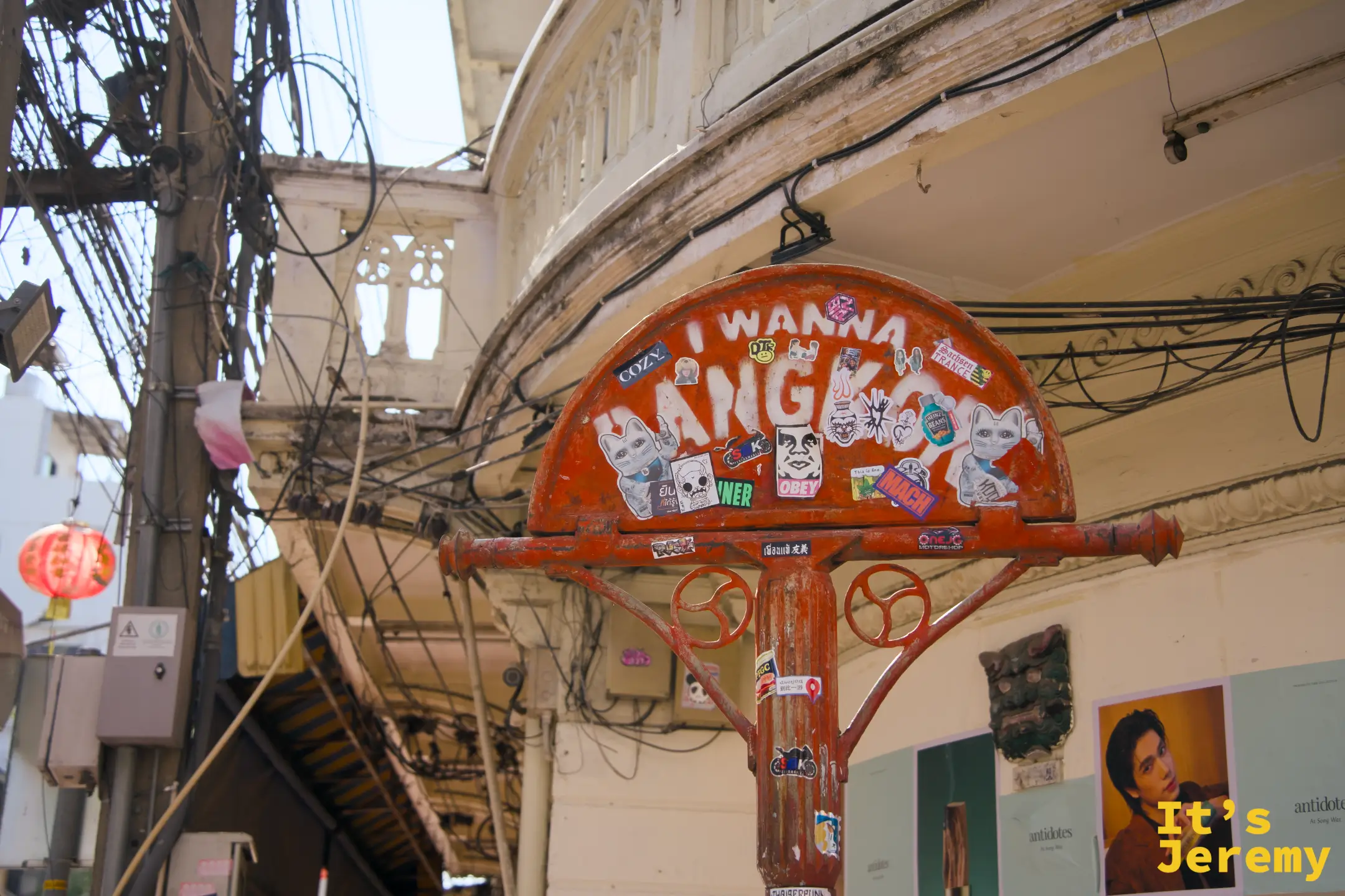 橘紅色半圓路標被貼紙全面覆蓋，「I WANNA BANGKOK」噴字最為醒目，老街屋建築與紅燈籠為背景