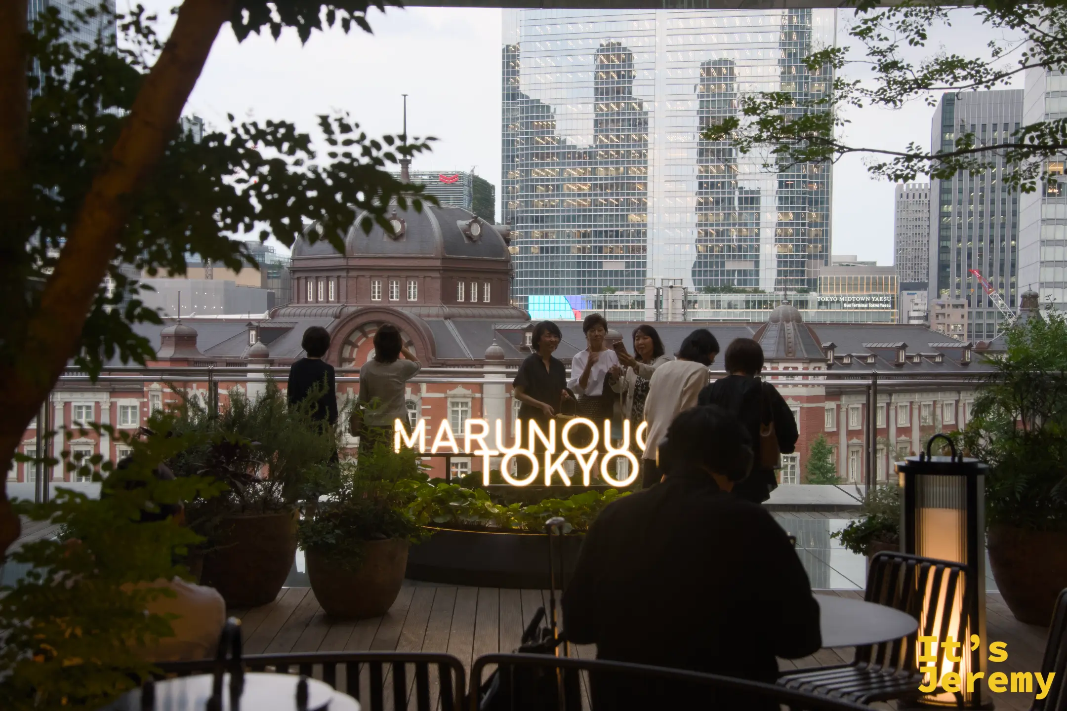MARUNOUCHI TOKYO 霓虹燈牌前，遊客聚集合影，背後是東京車站圓頂與摩天大樓