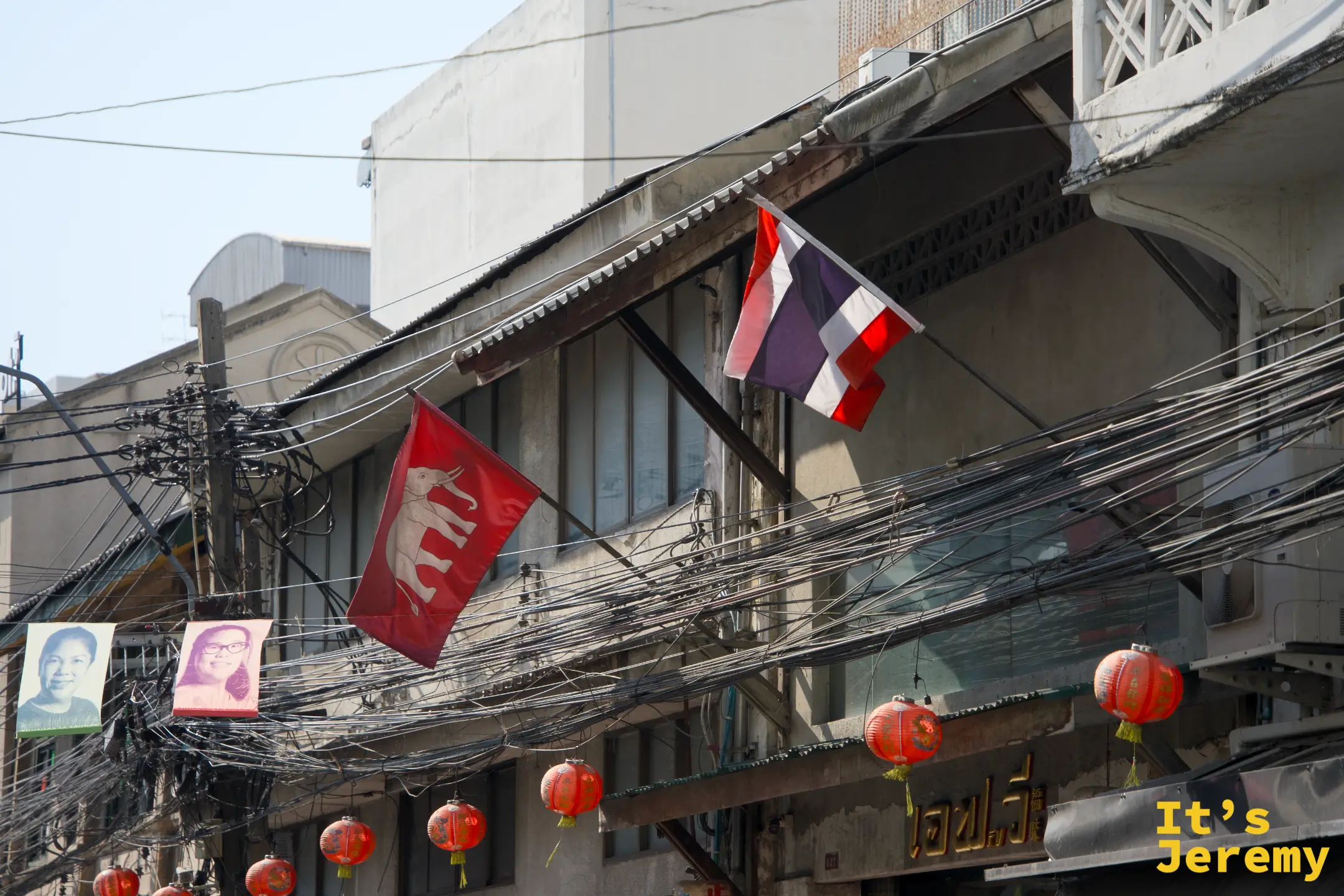 嵩越路老街屋建築一角：纏繞的電線叢、紅色布條旗幟與橘紅燈籠，百年街區的日常面貌