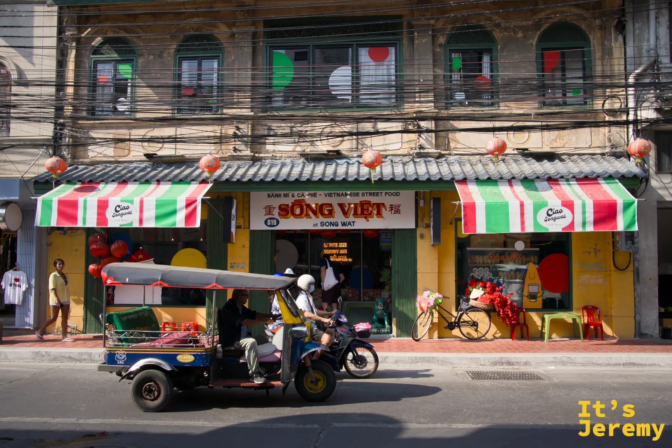「SÔNG VIỆT 越南街頭料理」餐廳外觀，紅白條紋遮陽棚，一輛嘟嘟車從前方駛過