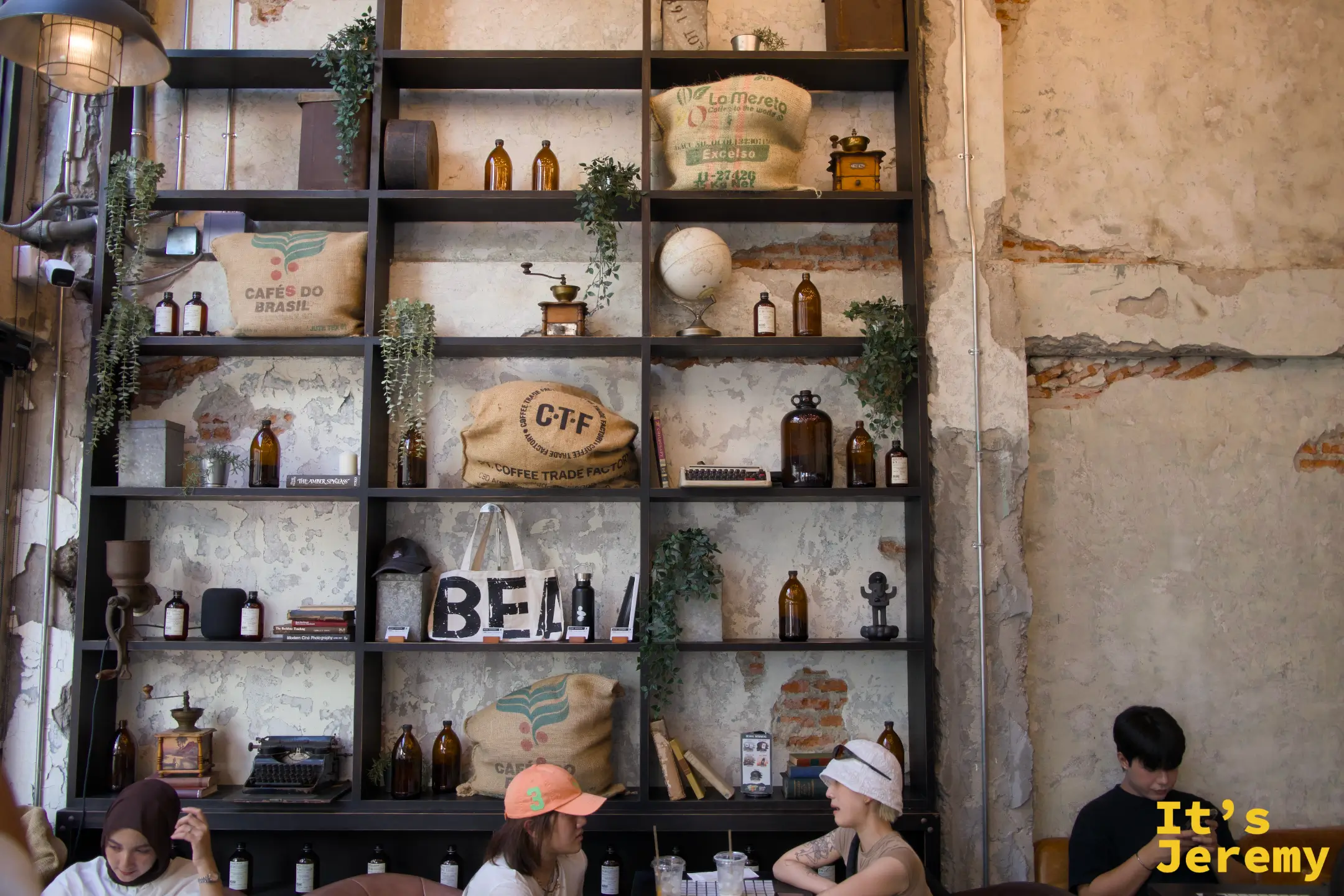 室內鐵架書牆:陳列麻布咖啡袋(Cafés do Brasil、CTF Coffee Trade Factory)、琥珀色玻璃瓶、打字機與地球儀,斑駁石灰牆面作為背景