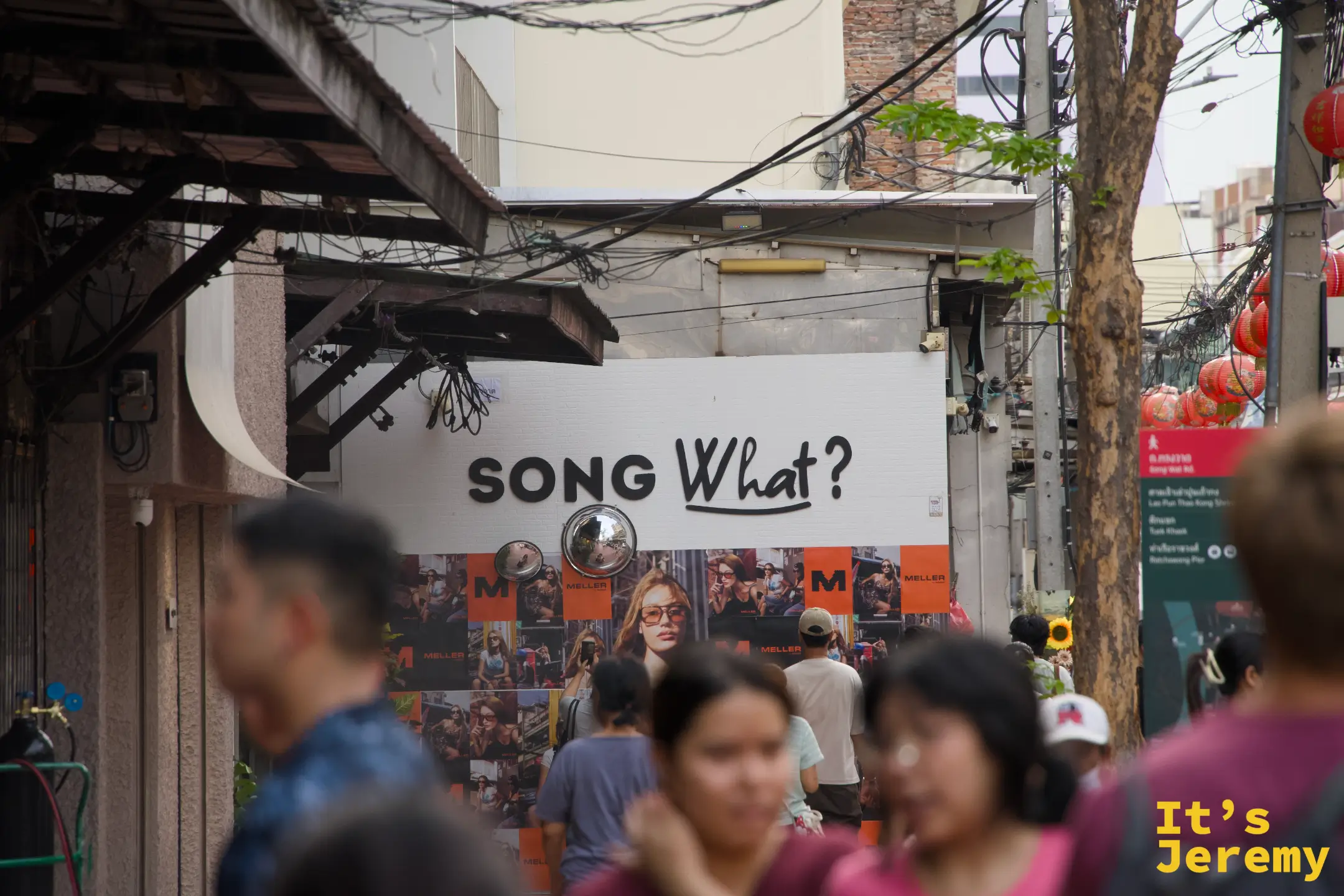「SONG What?」大字貼在巷口建築外牆,前景是人群,背後有紅燈籠和嵩越路路標