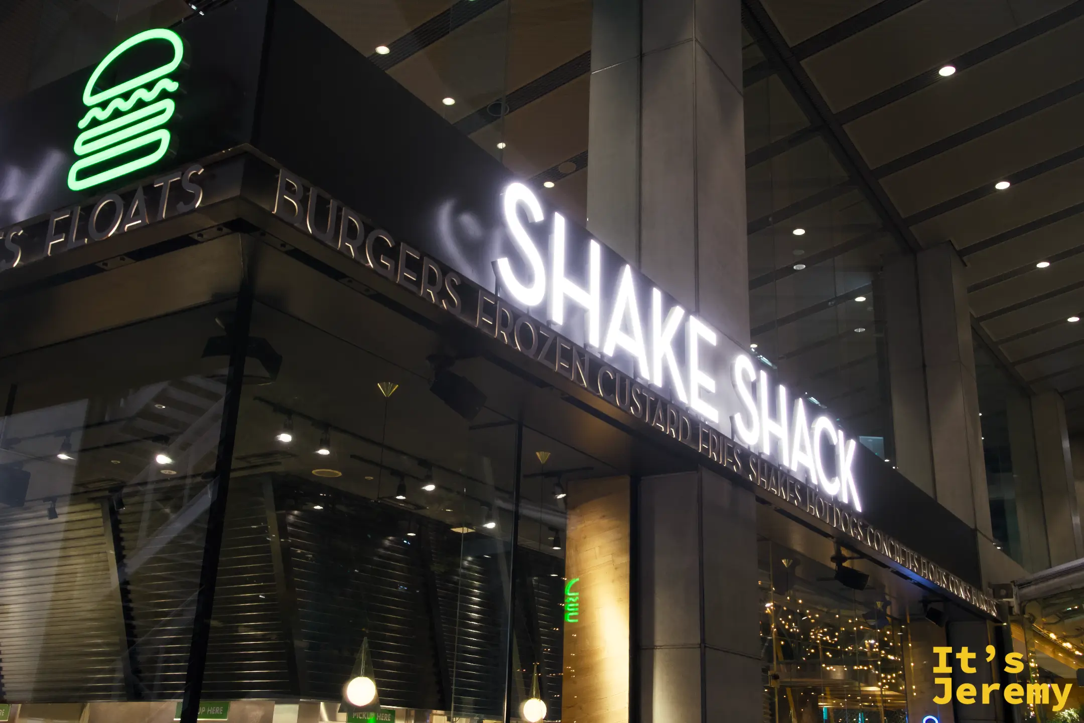 Shake Shack 東京國際論壇店店面招牌,白色燈箱大字與綠色霓虹漢堡 logo,夜間拍攝