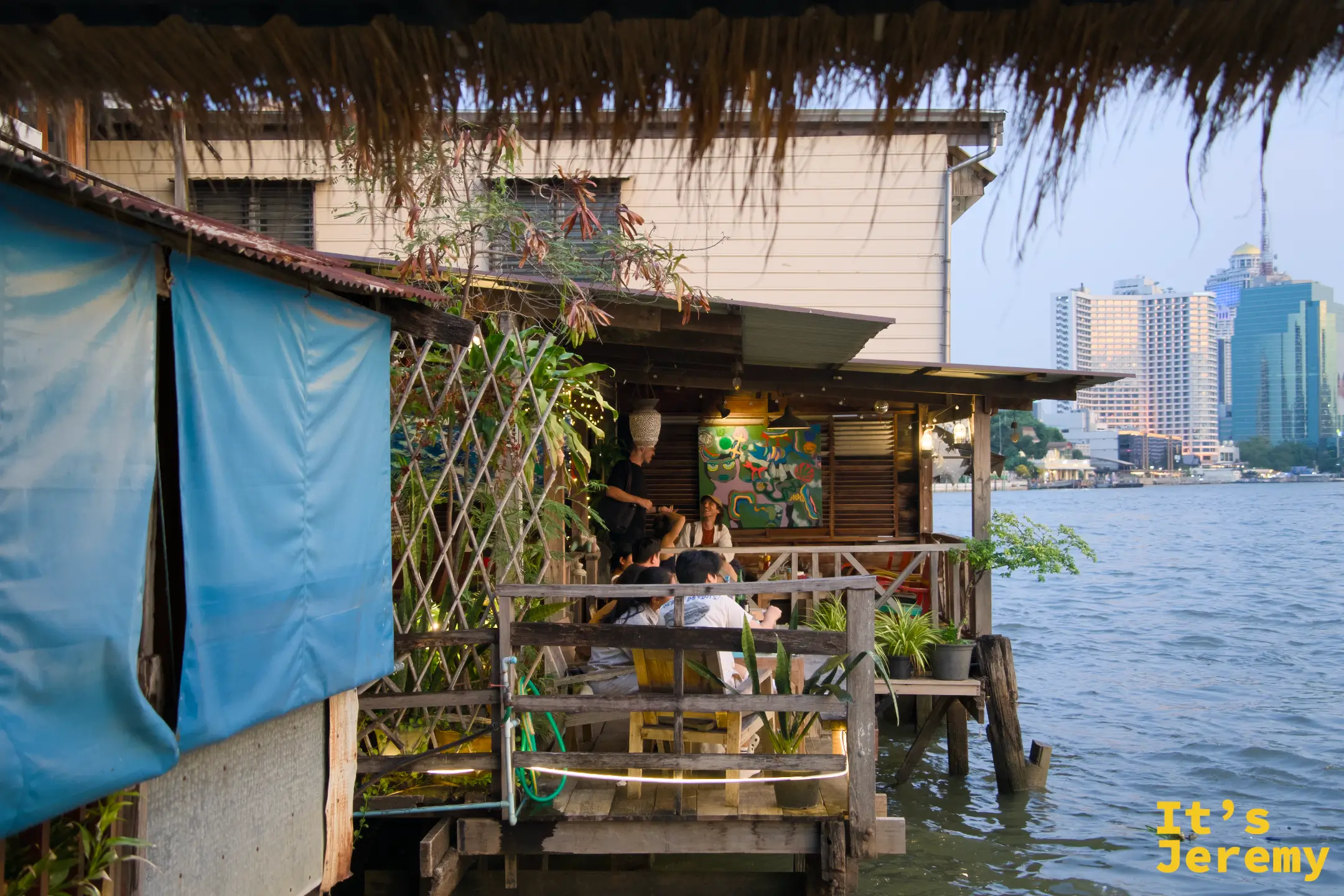 NAAM 1608 餐廳外觀，木製老屋結構緊靠昭披耶河，對岸可見曼谷市區高樓輪廓
