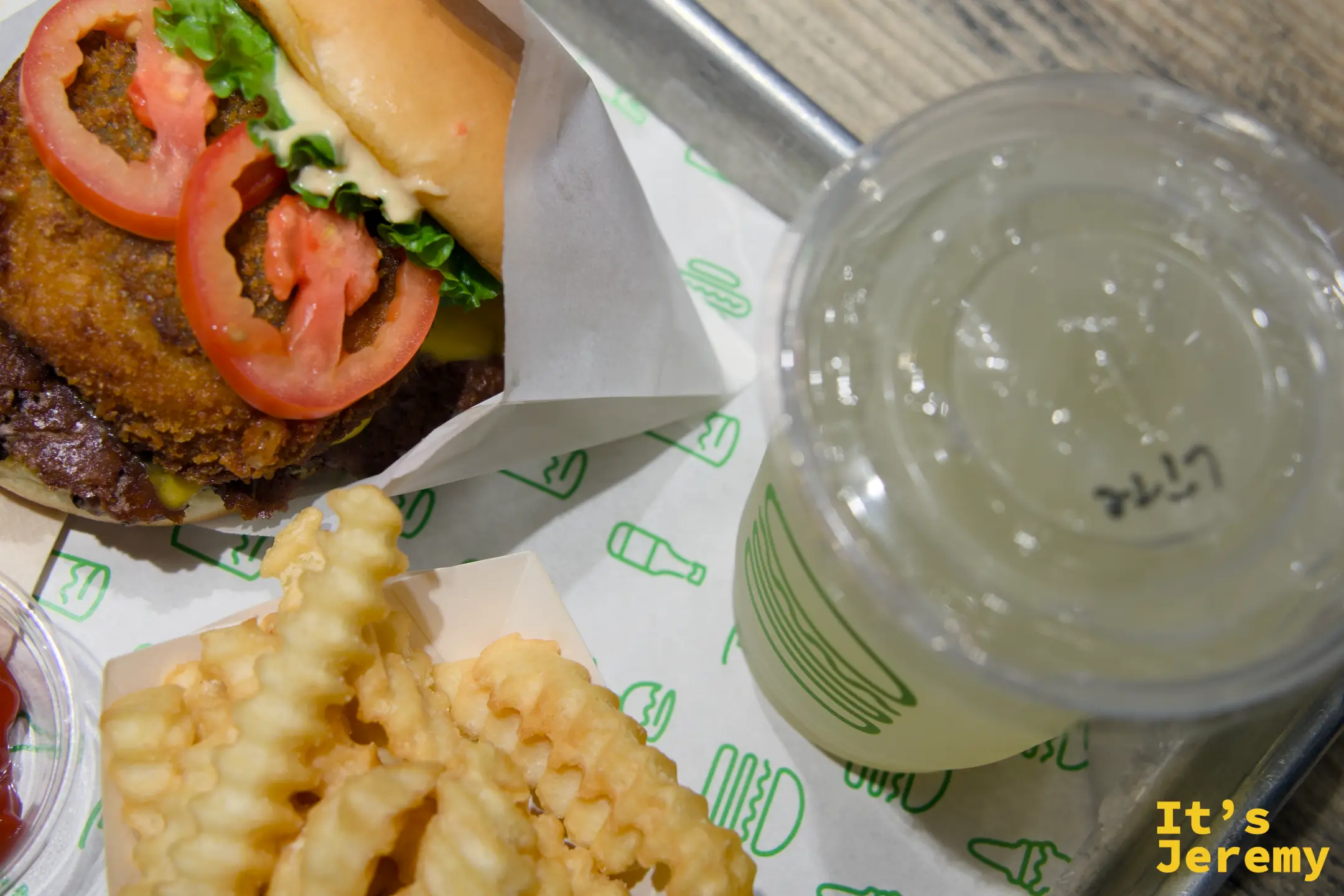 俯瞰角度的 ShackStack、波浪薯條與檸檬水,托盤鋪有 Shake Shack 品牌圖案紙