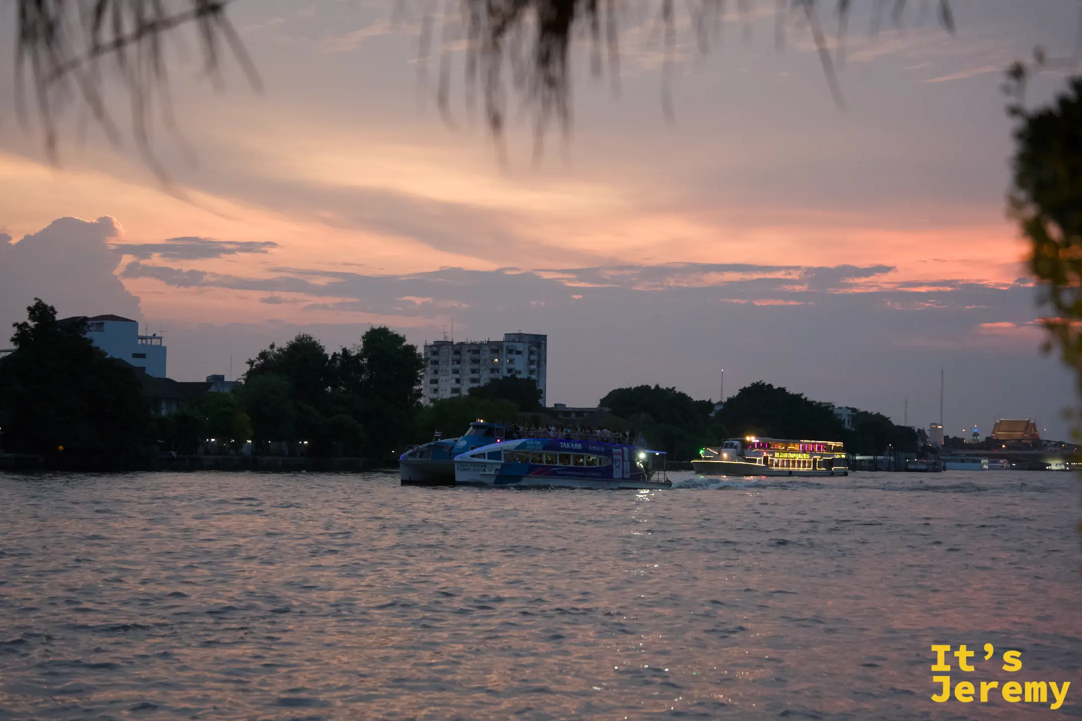 傍晚的昭披耶河,橙色夕陽映在水面,渡輪與觀光船緩緩駛過,河對岸市區燈光漸亮