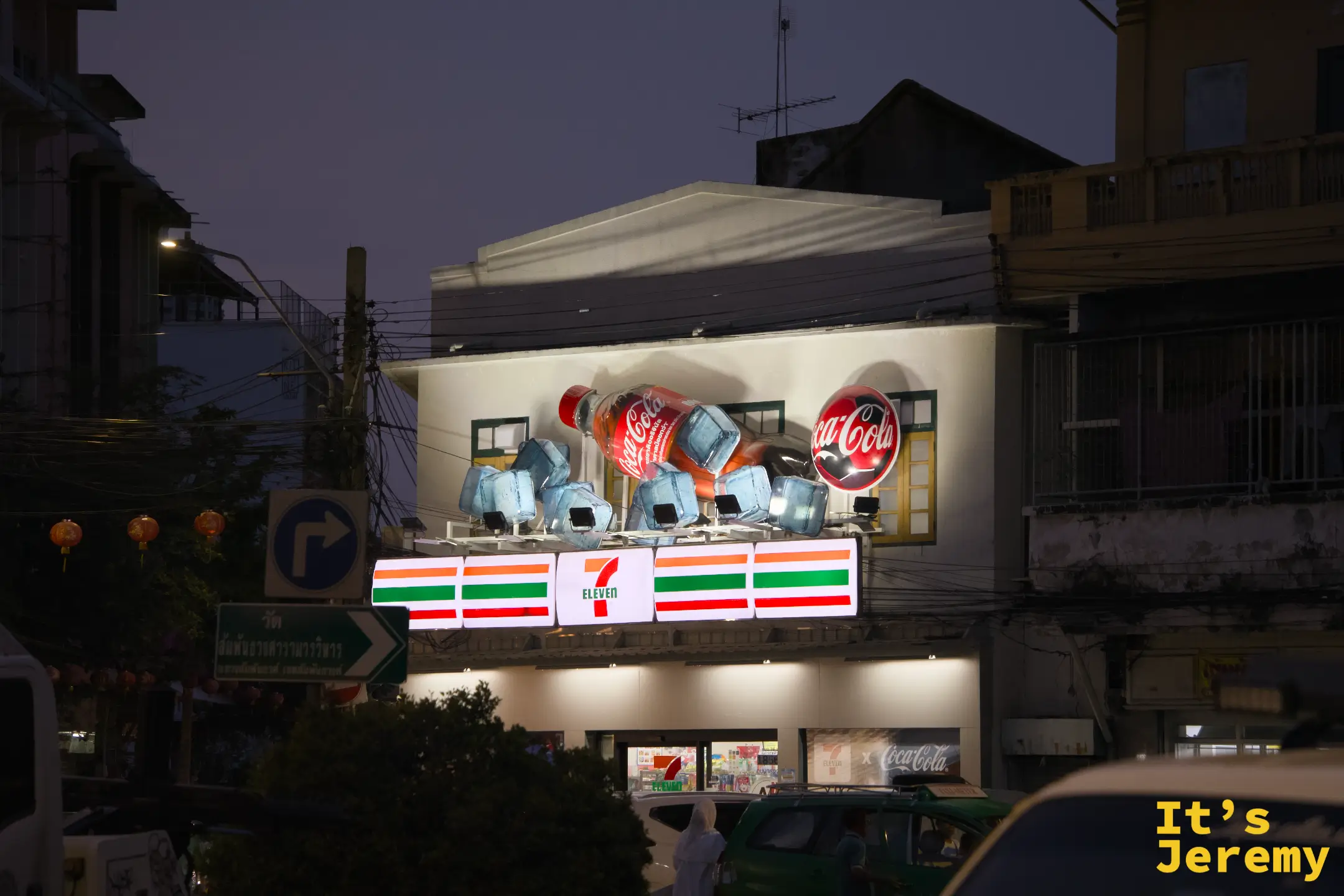 入夜後的 7-Eleven 建築:立體 Coca-Cola 玻璃瓶裝置在燈光下,左側可見紅燈籠