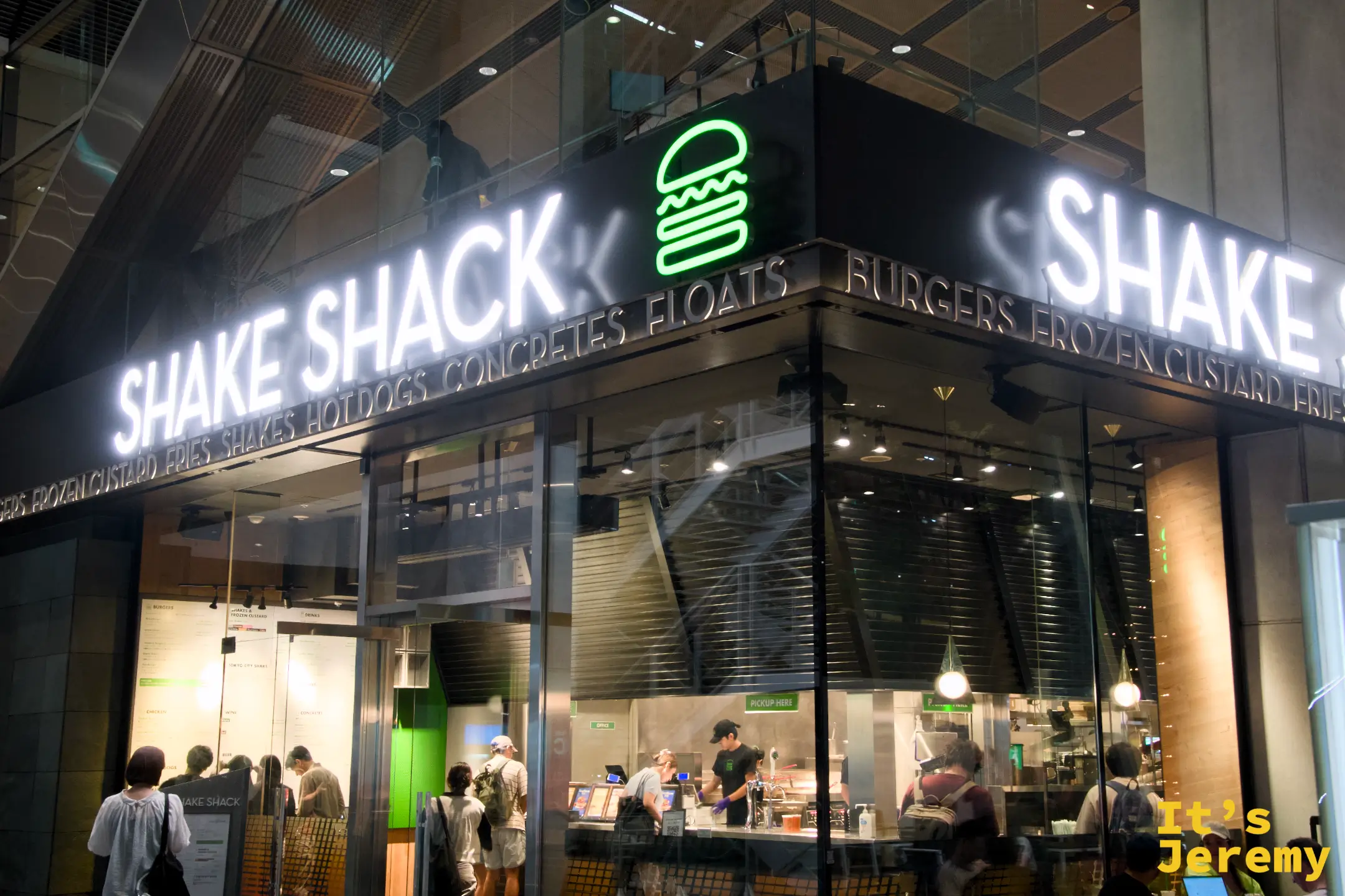 Shake Shack 東京國際論壇店夜間全景,玻璃門面、白色燈箱招牌與入場中的客人